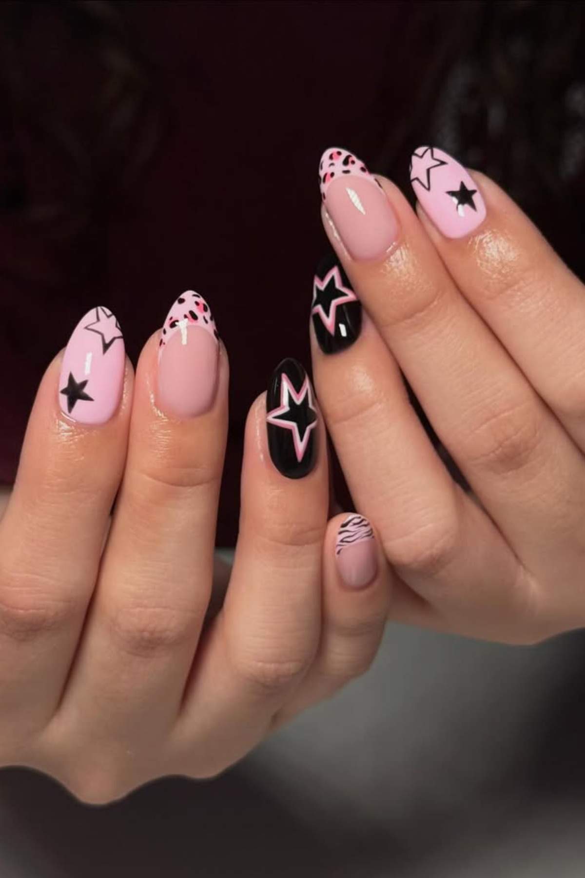 Close-up of hands with pink and black manicured nails featuring star designs and abstract patterns.