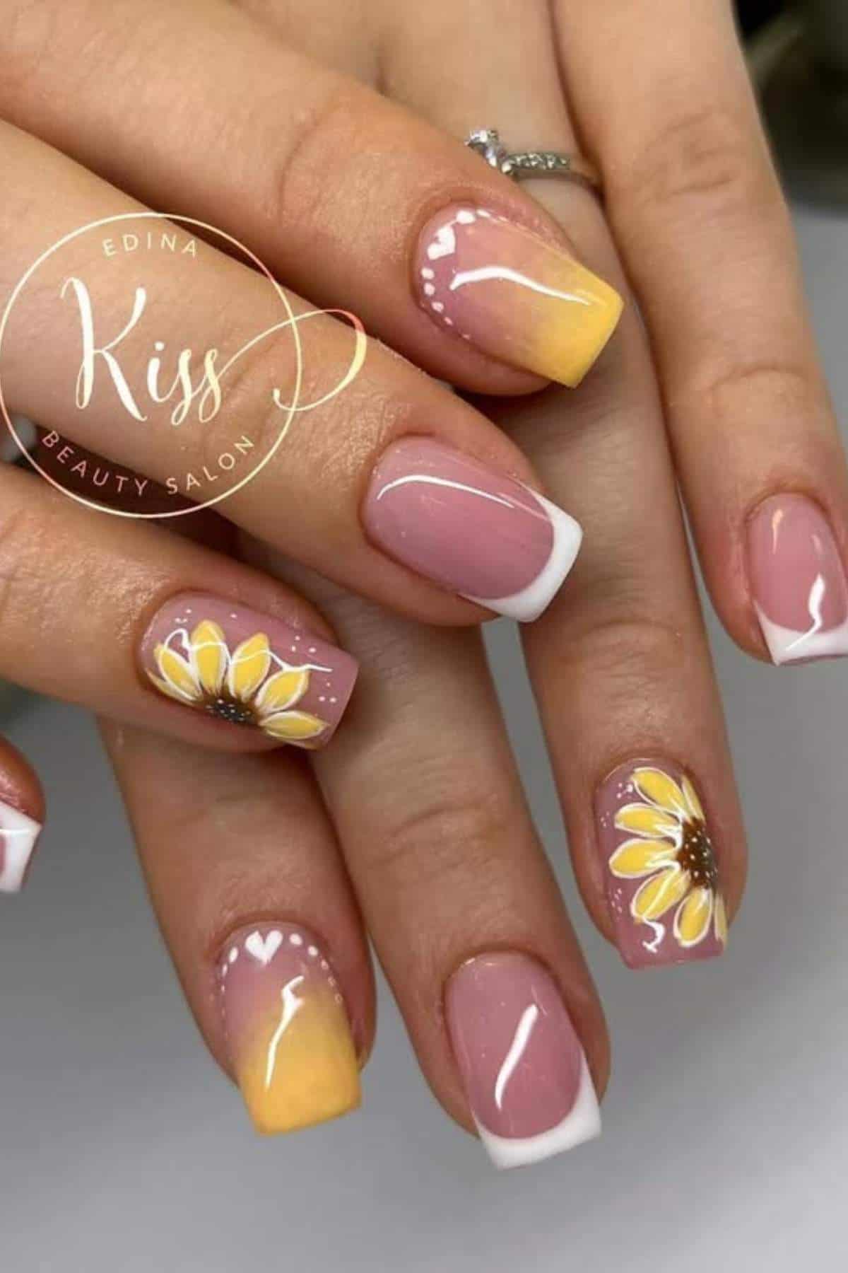 Close-up of hands with manicured nails featuring yellow ombre tips, white French tips, and sunflower designs on a few accent nails.
