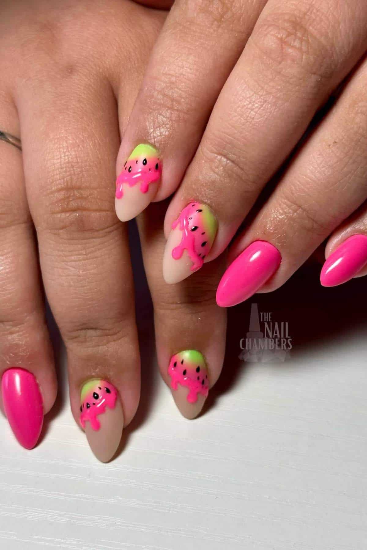 Close-up of hands with manicured nails featuring a pink and green watermelon design with black seeds, alongside solid hot pink nails.