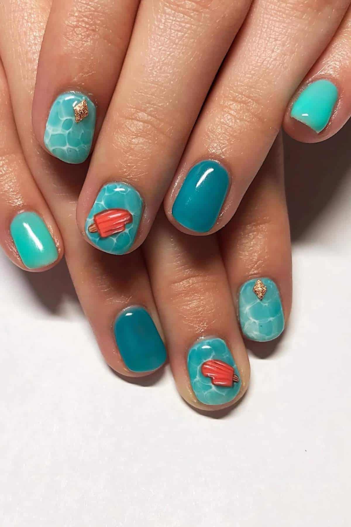Hands with short, oval-shaped nails painted in blue and turquoise shades, some with a pool water pattern and accents of small red flippers and gold details.