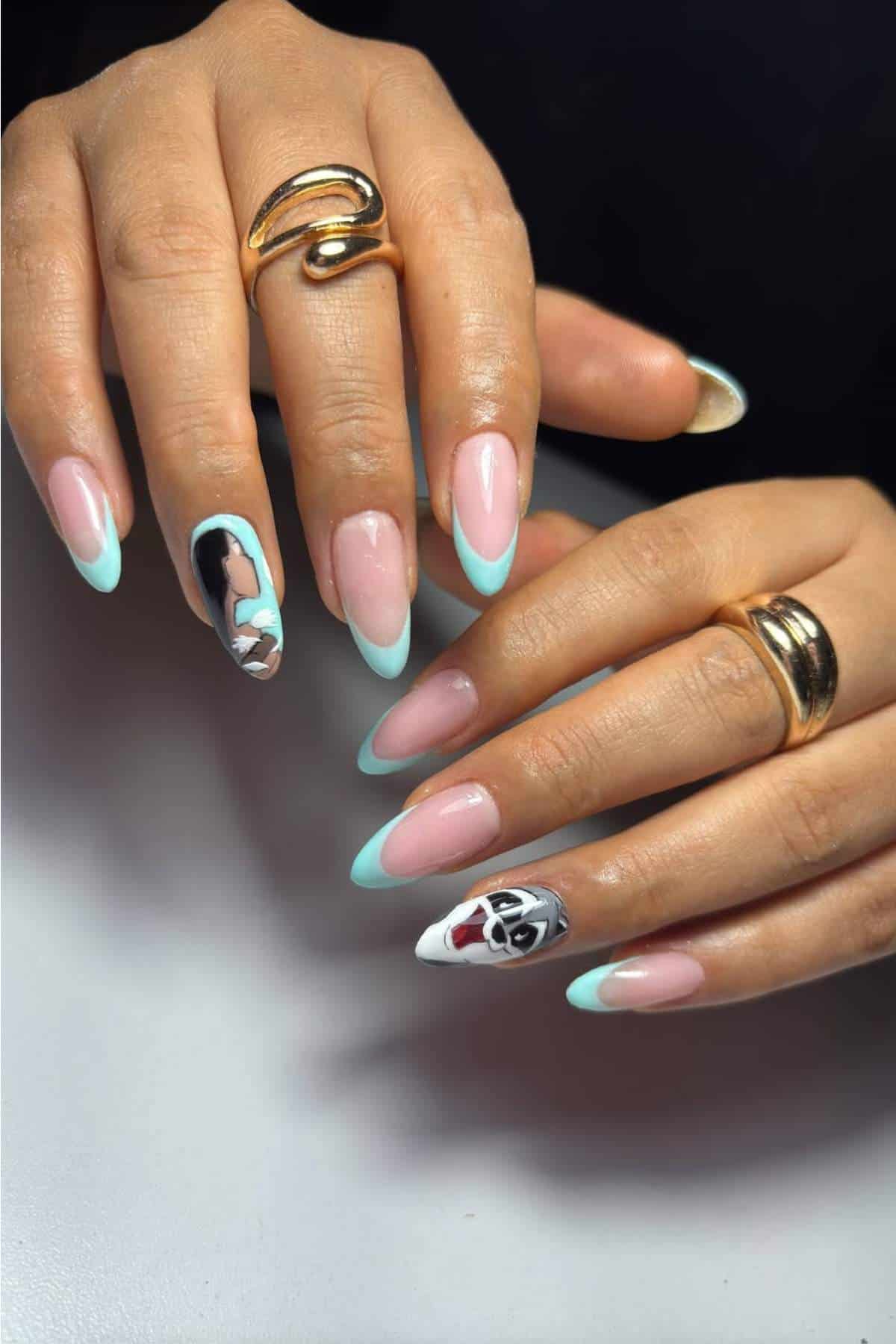 A person with almond-shaped nails featuring light blue French tips and abstract face designs on the ring fingers, wearing gold rings.