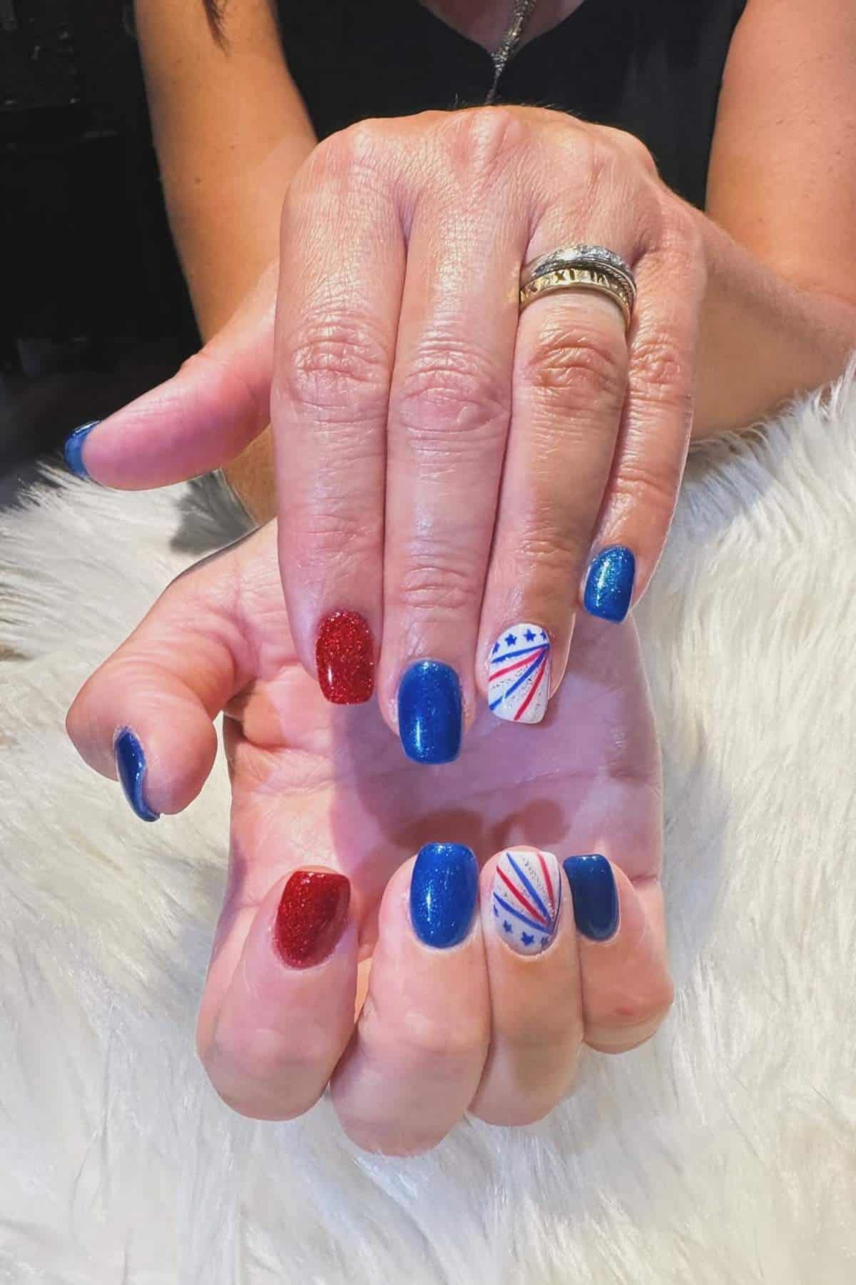 Hands with a patriotic-themed manicure: red glitter, blue, and white nails with red and blue stripes and stars.