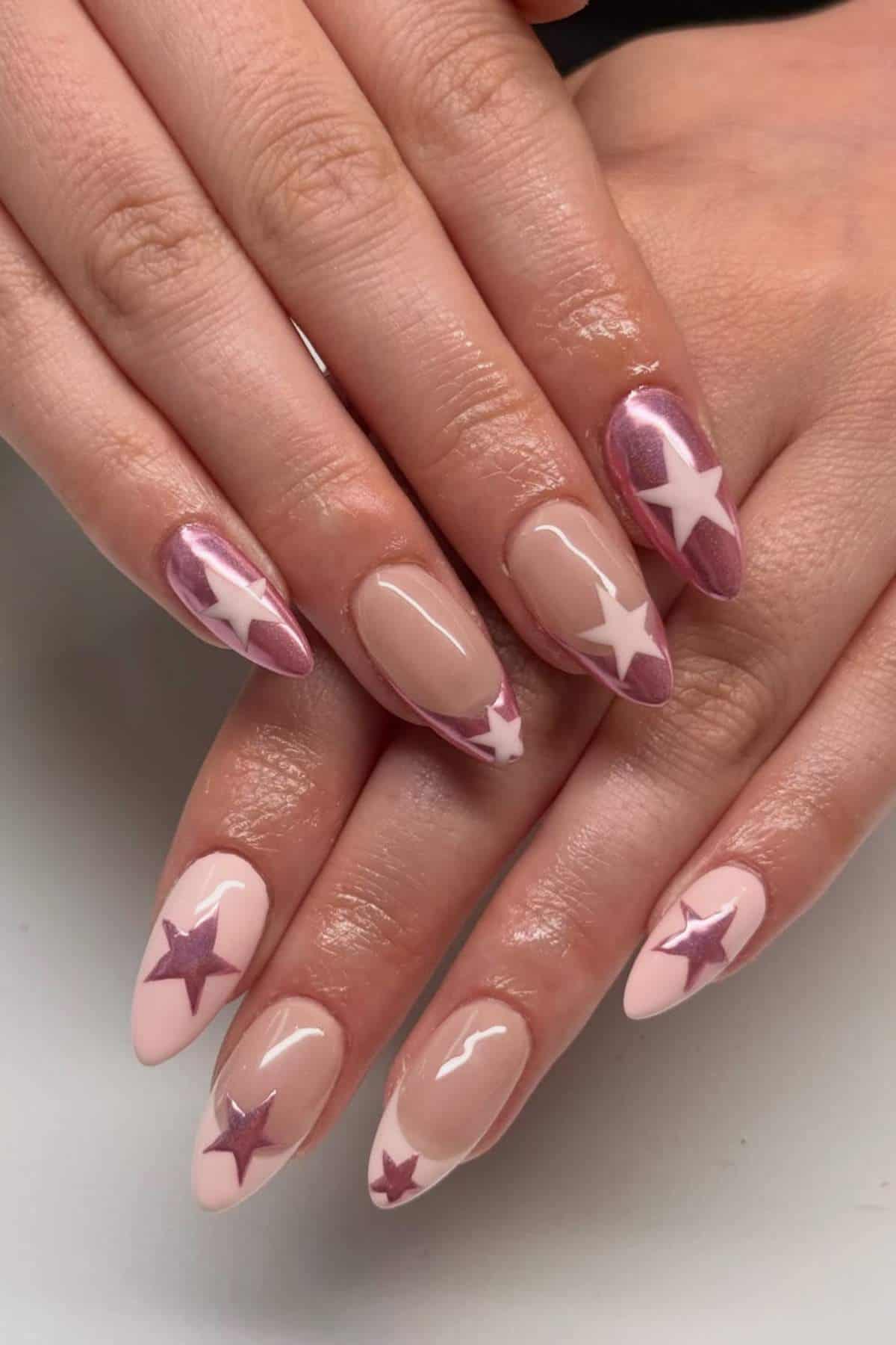 Hands with almond-shaped nails featuring a nude base, accented with large pink and white star designs on each nail.