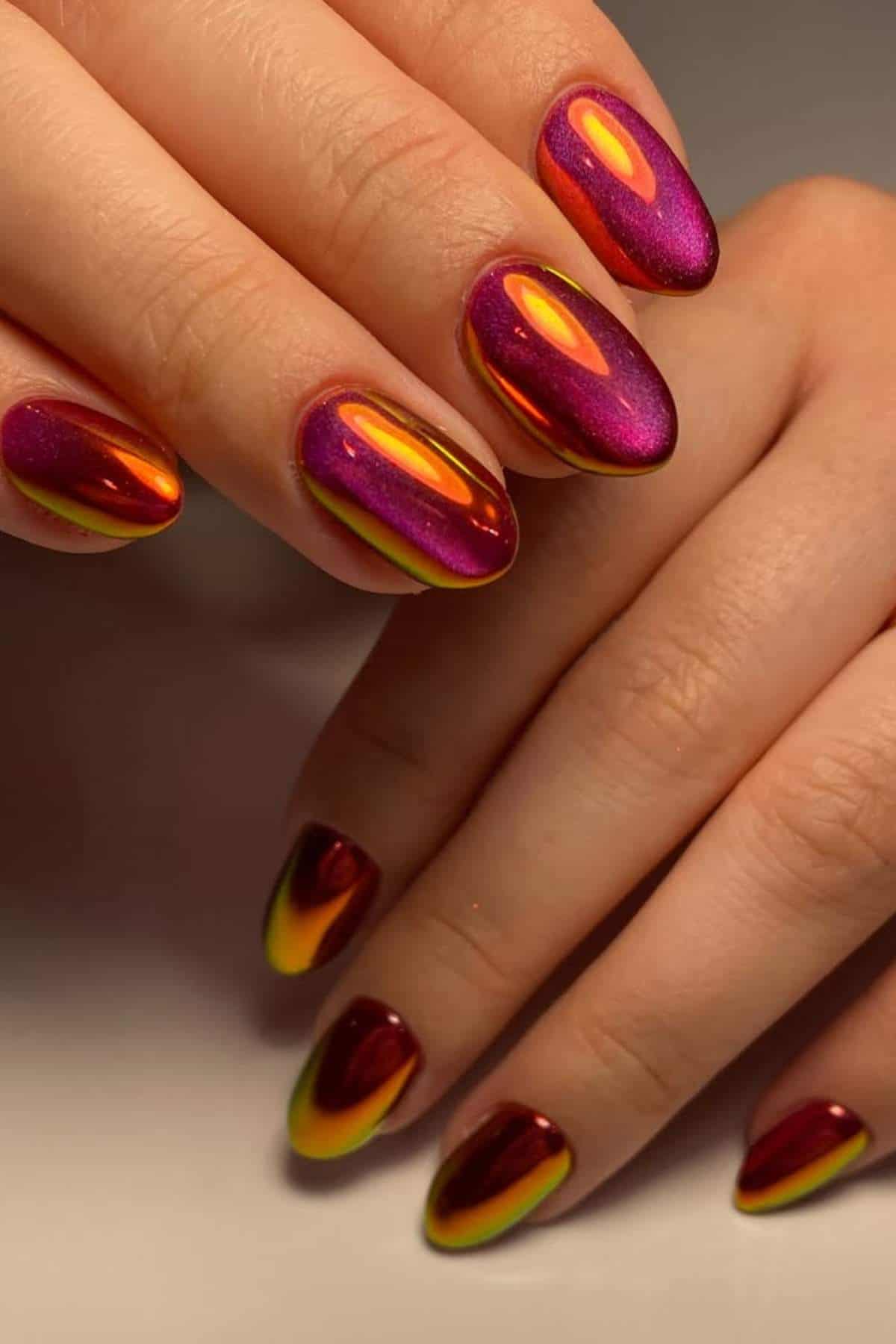 A hand with almond-shaped nails featuring a shiny gradient design in metallic red, yellow, and purple tones.