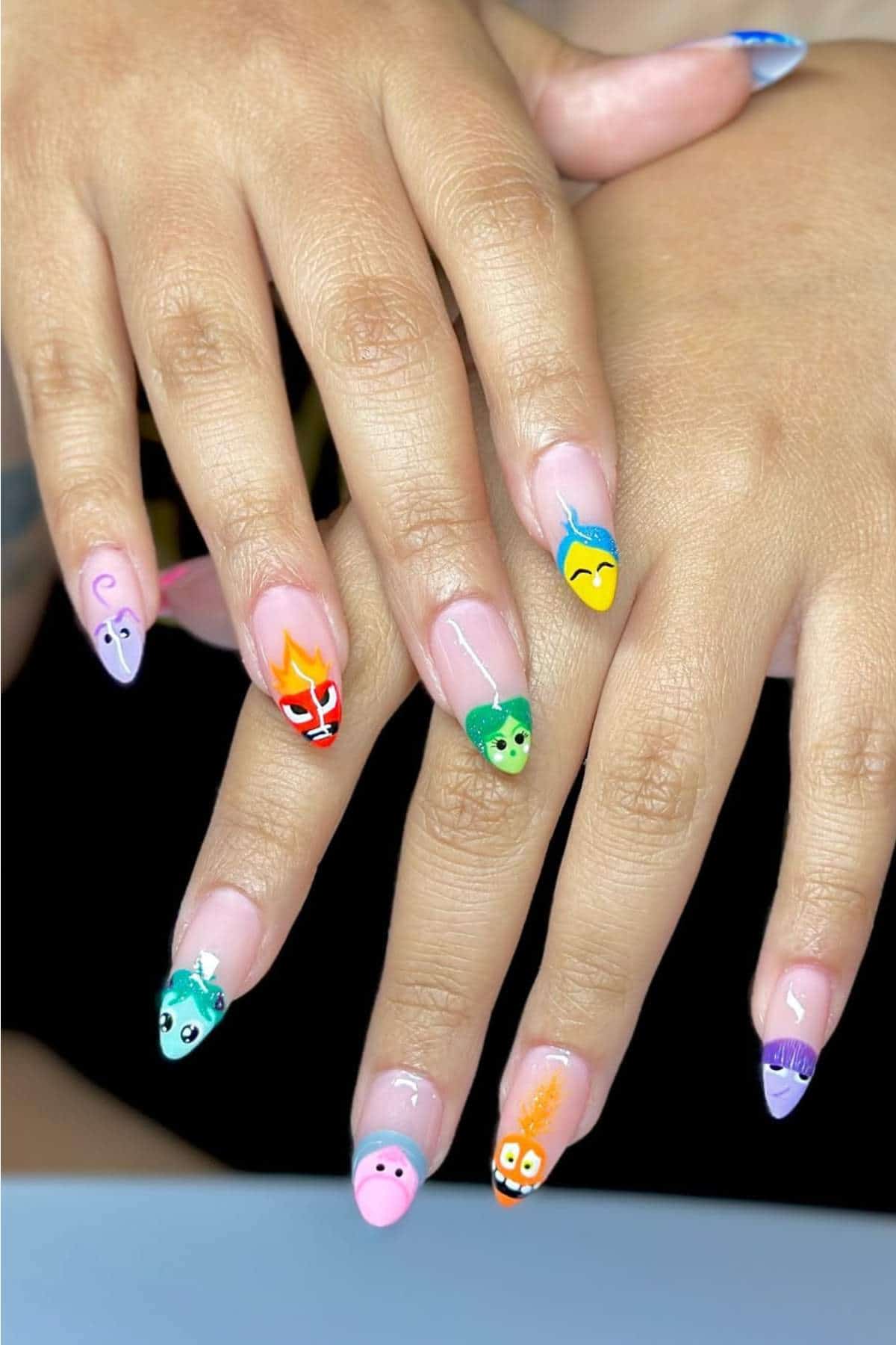 A pair of hands with long nails, each painted with a different cartoon-style face or design in various bright colors.