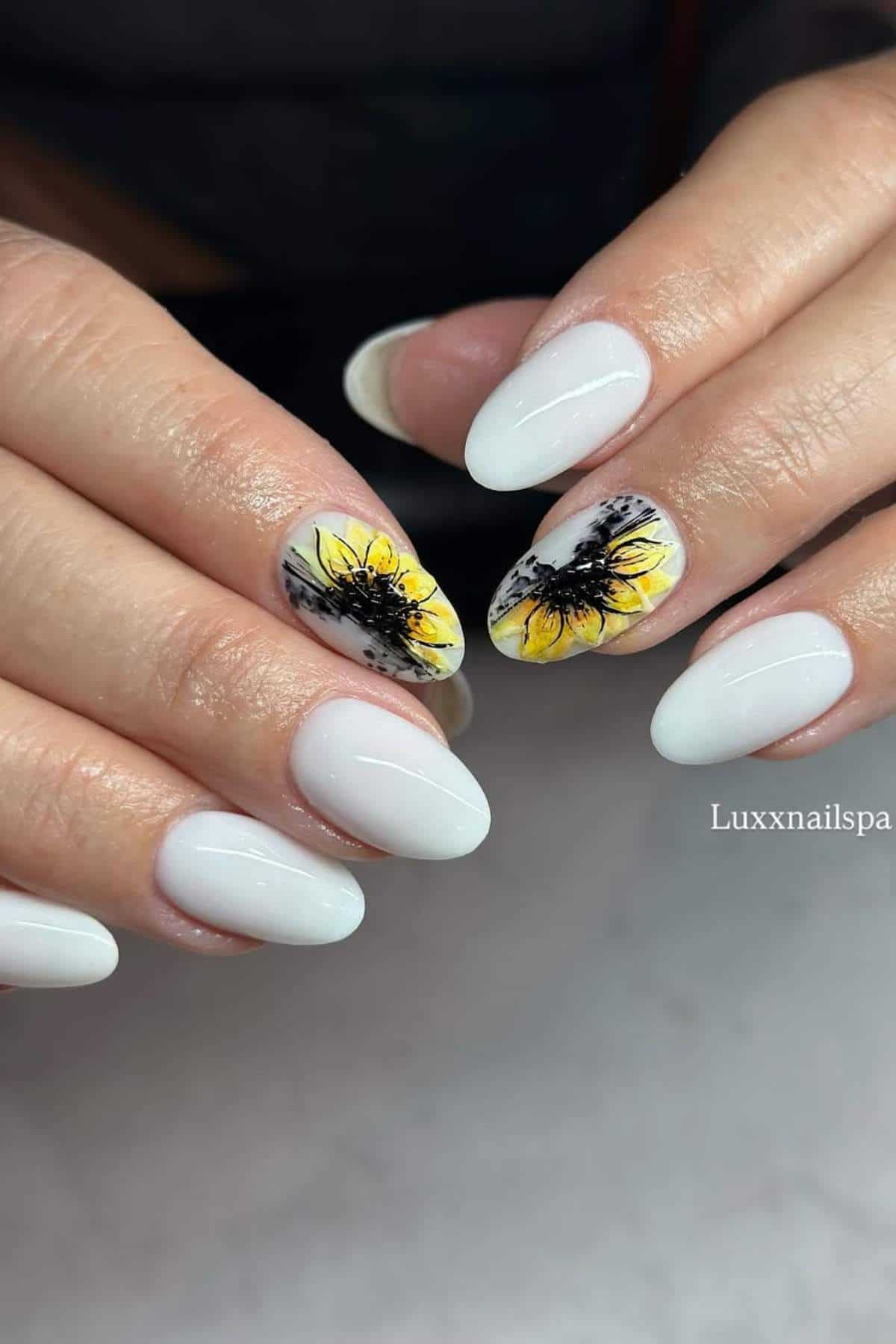 Hands with white almond-shaped nails; two accent nails feature detailed yellow sunflower designs.