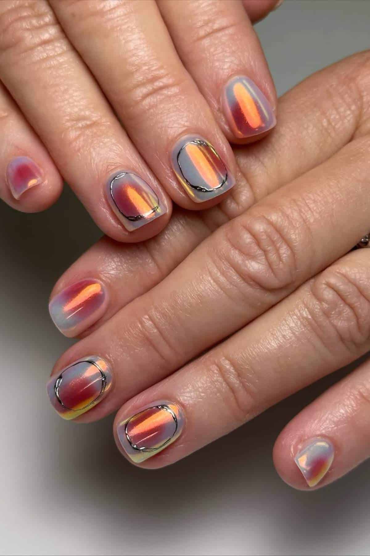 Close-up of hands with short, rounded nails featuring an orange, yellow, and pink gradient design with fine black and gold line accents.