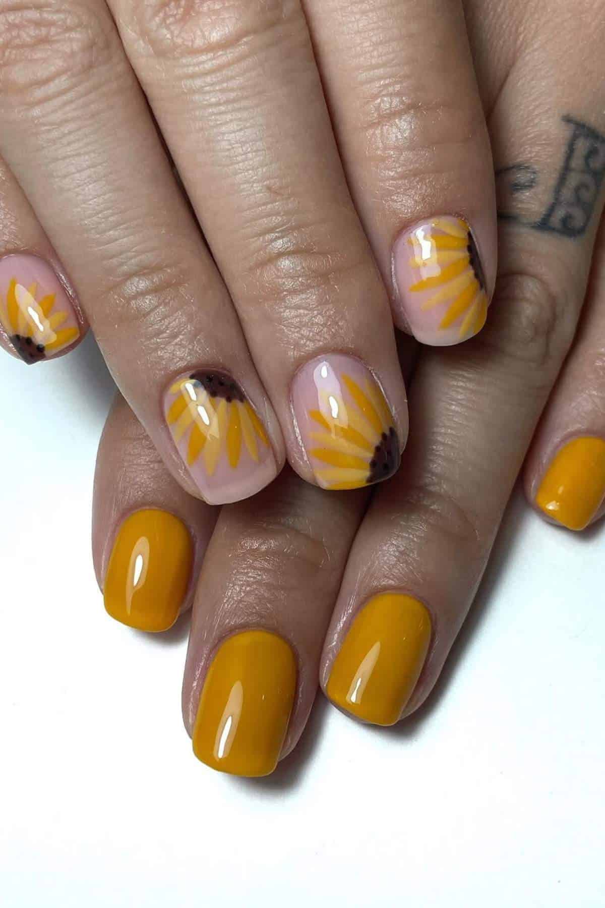 Hands with manicured nails featuring yellow polish and accent nails with sunflower petal designs on a nude base.
