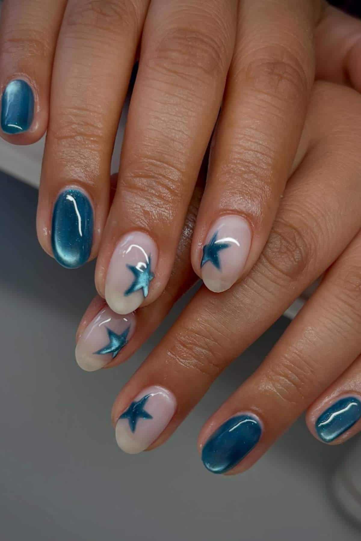Hands with manicured nails; some nails are painted metallic blue while others are nude with blue star designs.