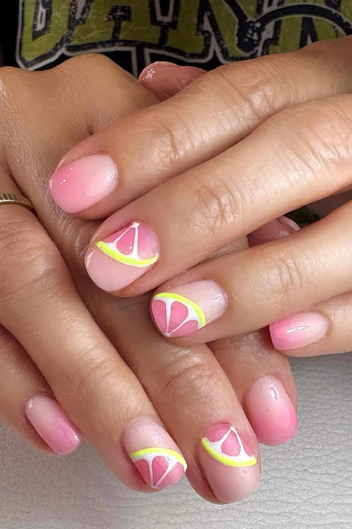 Hands with pink manicured nails, some featuring citrus fruit slice designs in white, yellow, and pink colors.