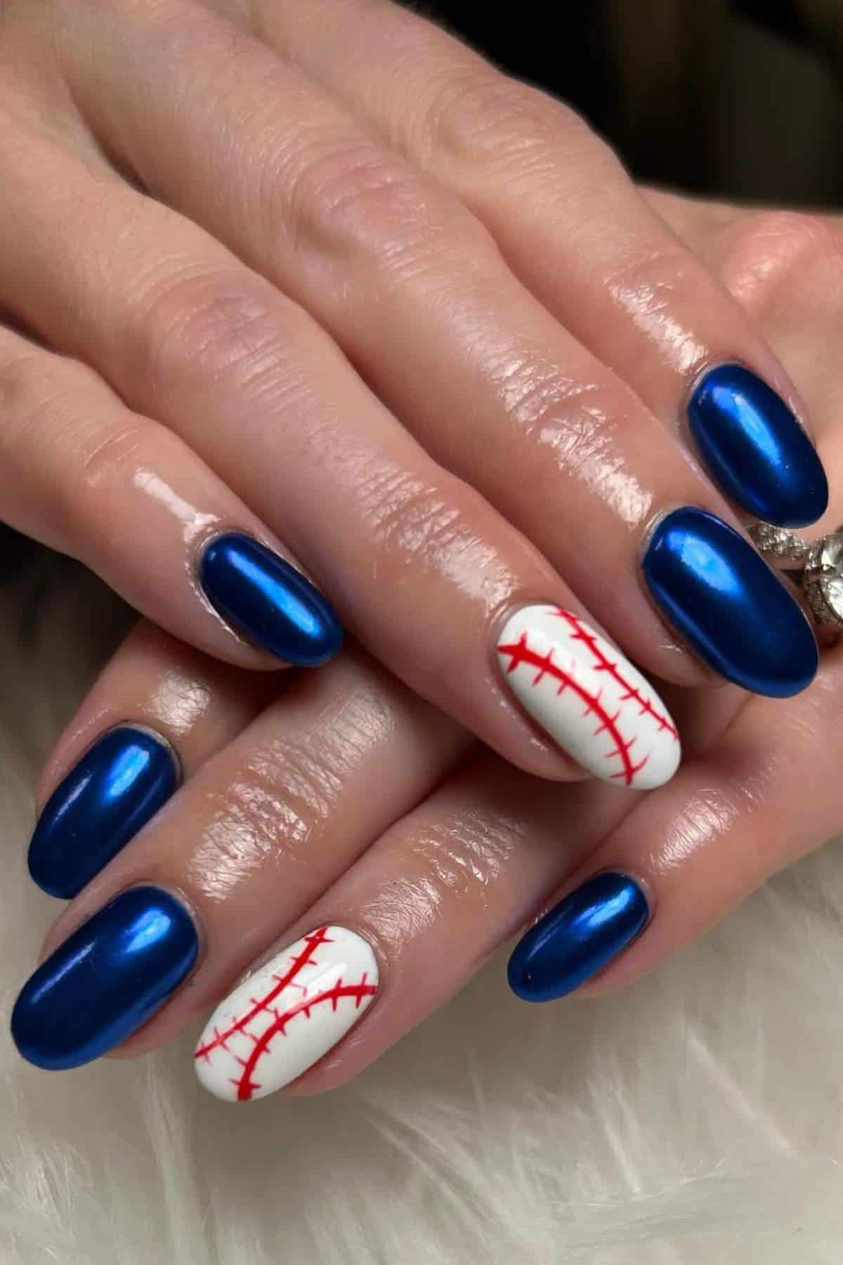 A hand with oval-shaped blue metallic nails, except for two nails painted white with red stitching resembling a baseball design.