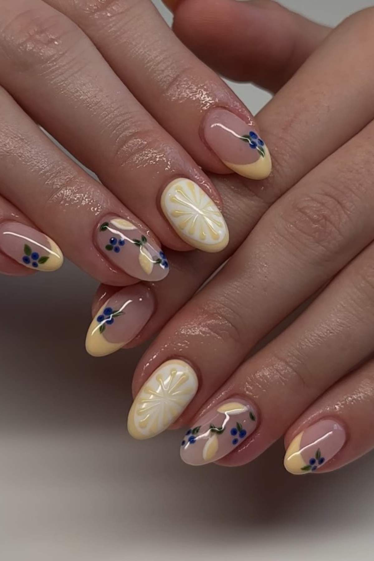 Hands with almond-shaped nails featuring yellow French tips, floral designs, and accent nails with yellow and white flower patterns on a glossy nude base.