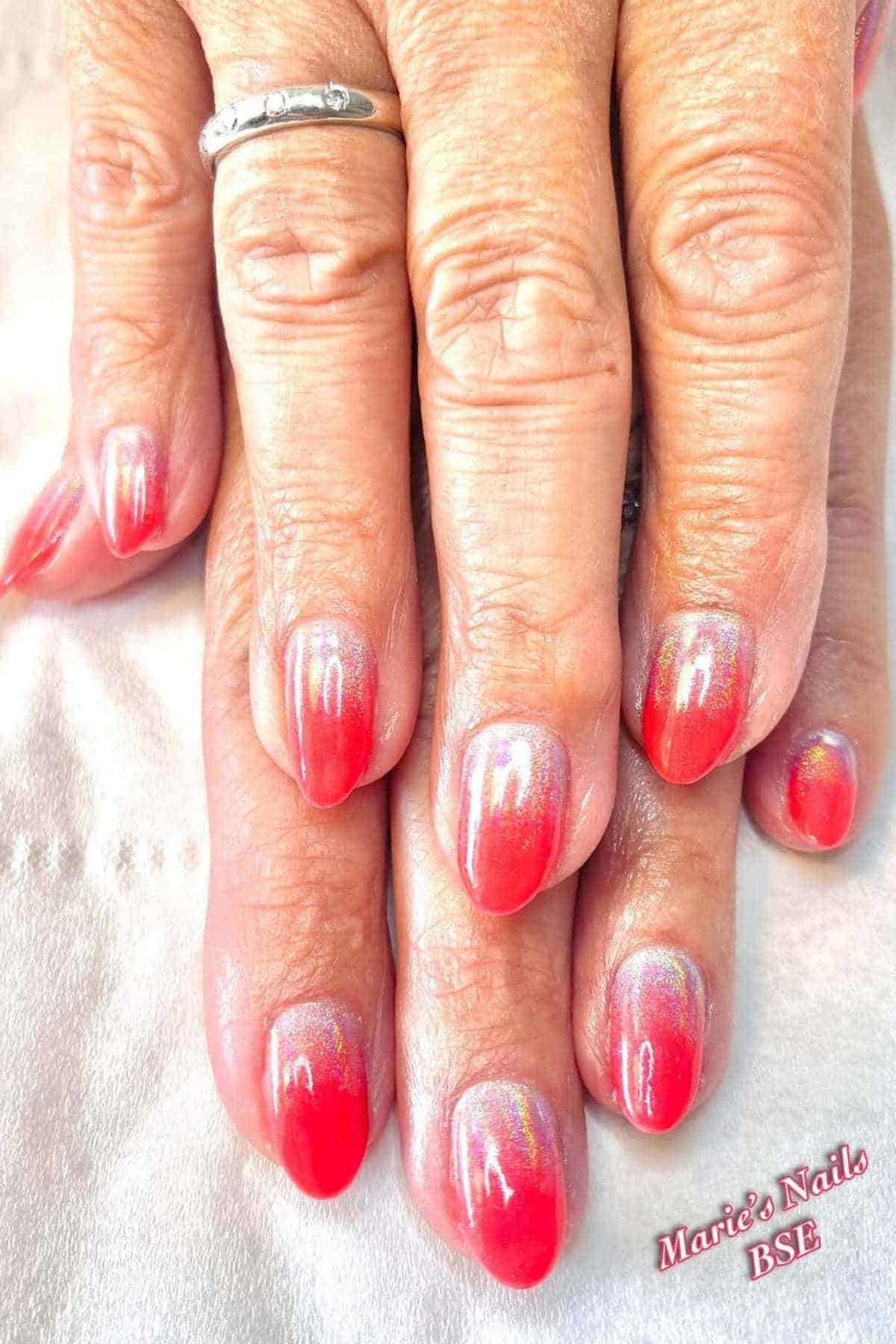 Close-up of hands with red and pink ombre gel manicure, some shimmer effect visible; wearer has a silver ring on one finger.