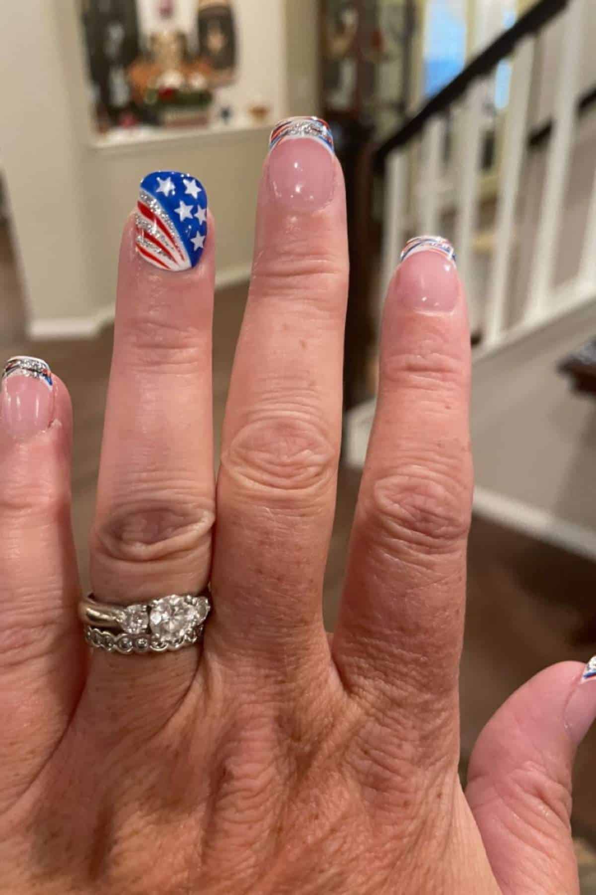 Close-up of a hand showing nails painted with an American flag design and glitter accents.