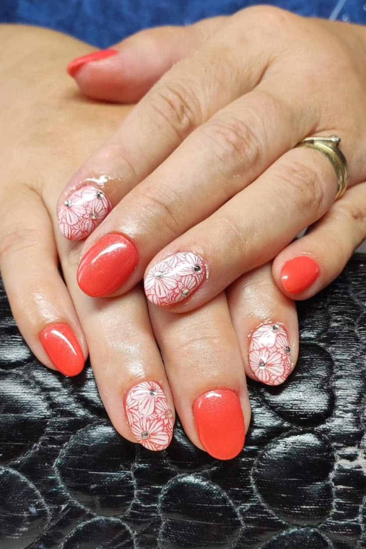 Hands with coral-colored nails, some featuring white floral designs, resting on a textured black surface.
