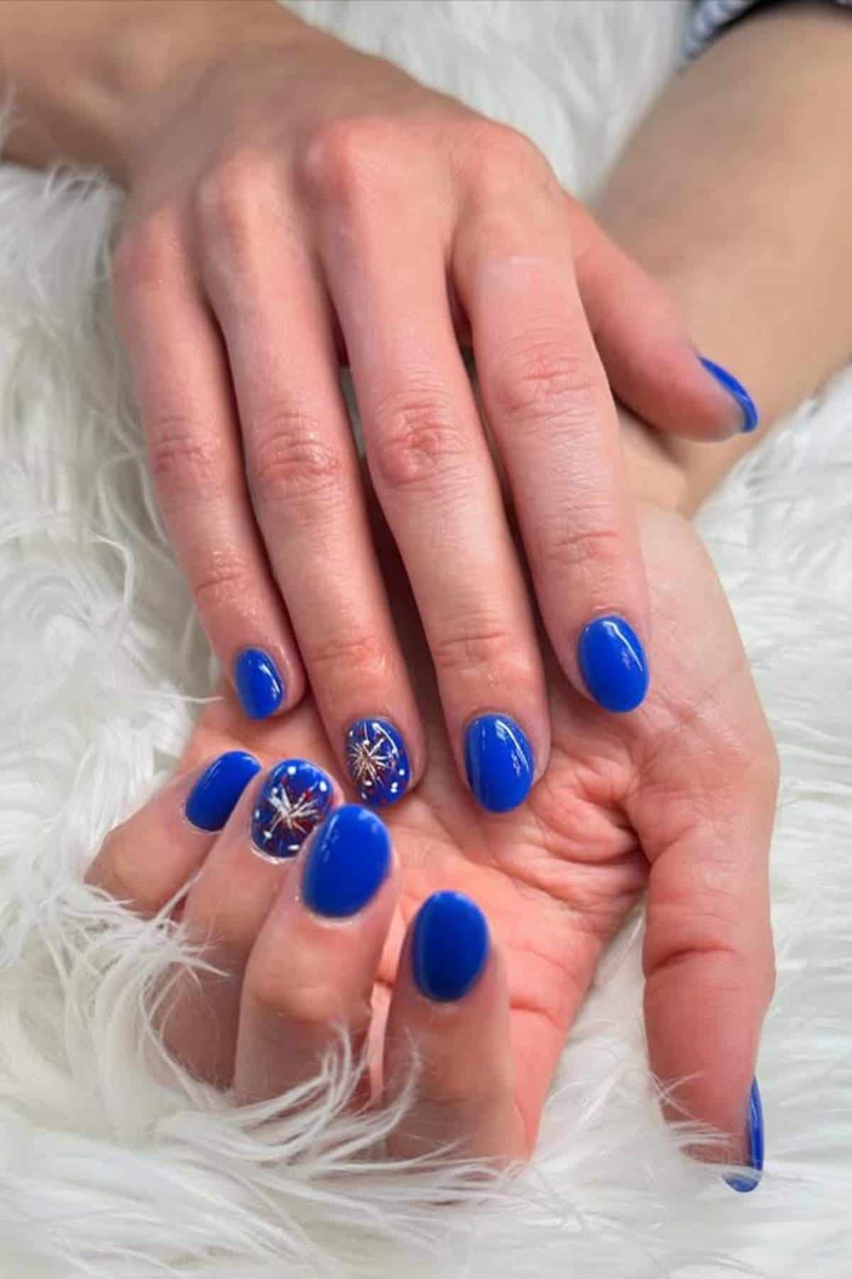 Short, oval nails with a bright blue polish and white accent nails featuring red and white starburst designs.
