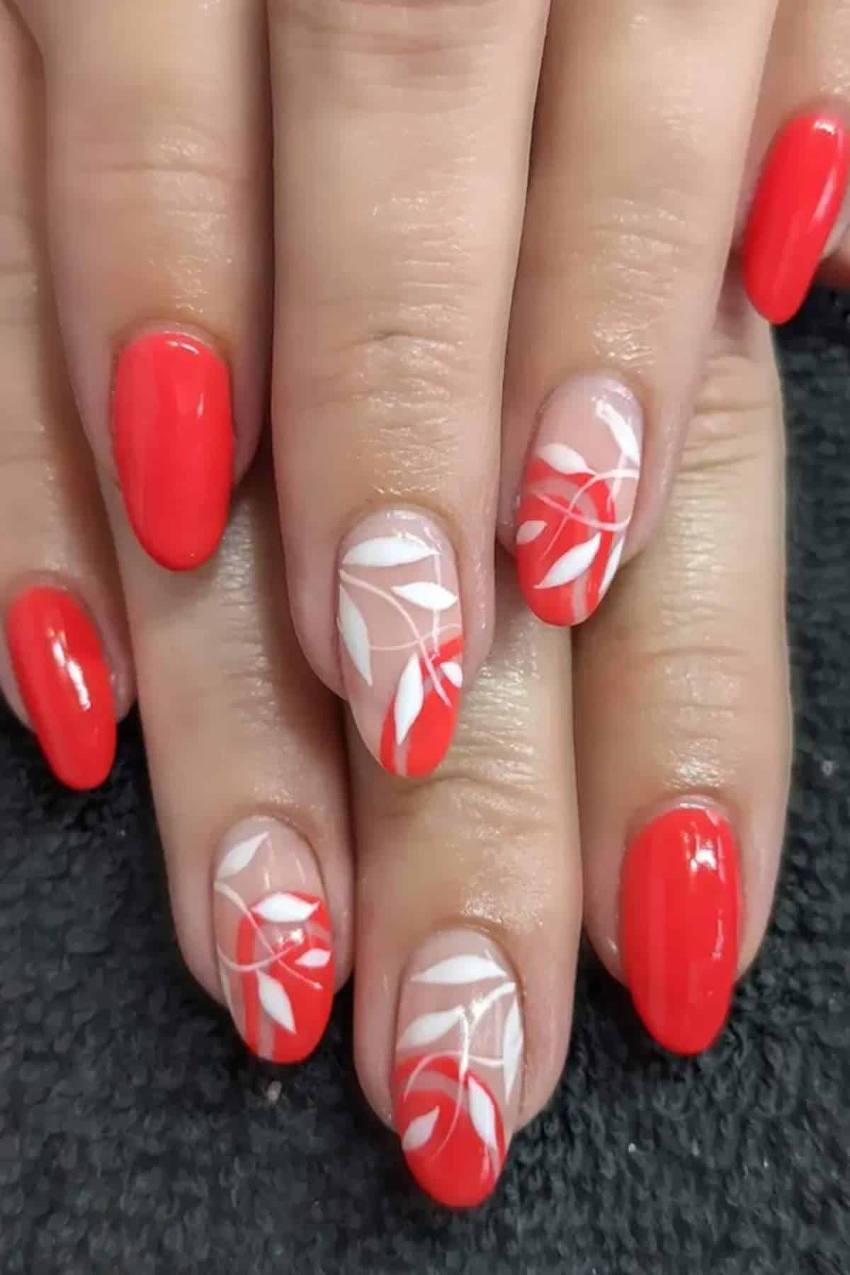 Hands with red painted nails; two nails on each hand have a nude base with white and red leaf designs.