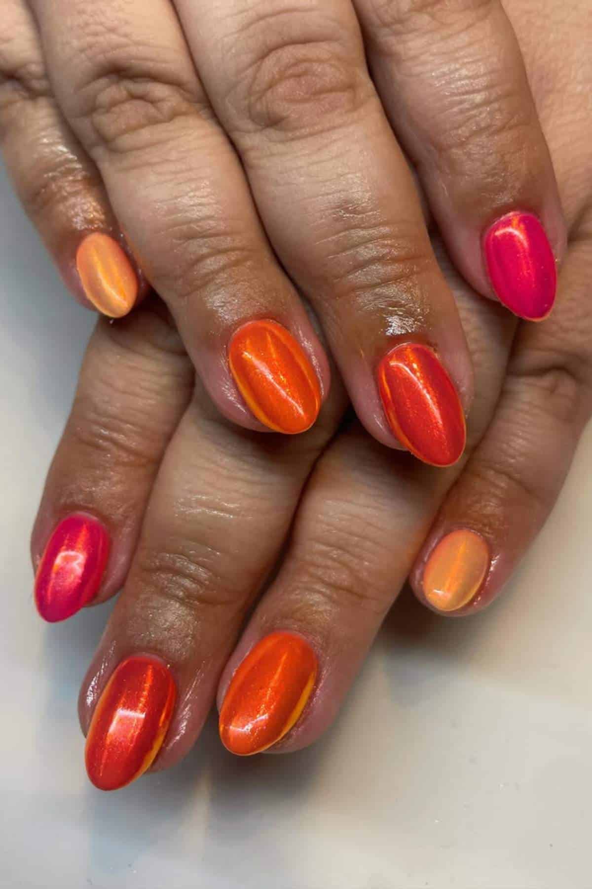 A hand with manicured nails painted in vibrant shades of pink, orange, and peach with a glossy finish.
