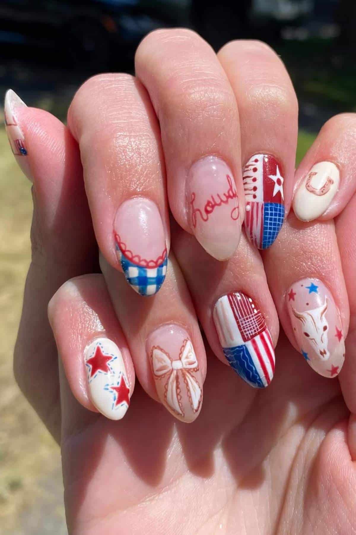 A hand with long, almond-shaped nails featuring western-themed nail art, including stars, checkered patterns, a bow, cowgirl hat, and the word "Rough.