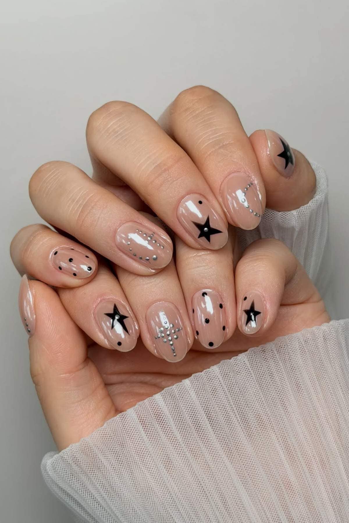 A hand with short, nude-colored nails featuring black stars, silver lines, and black dots as nail art accents.