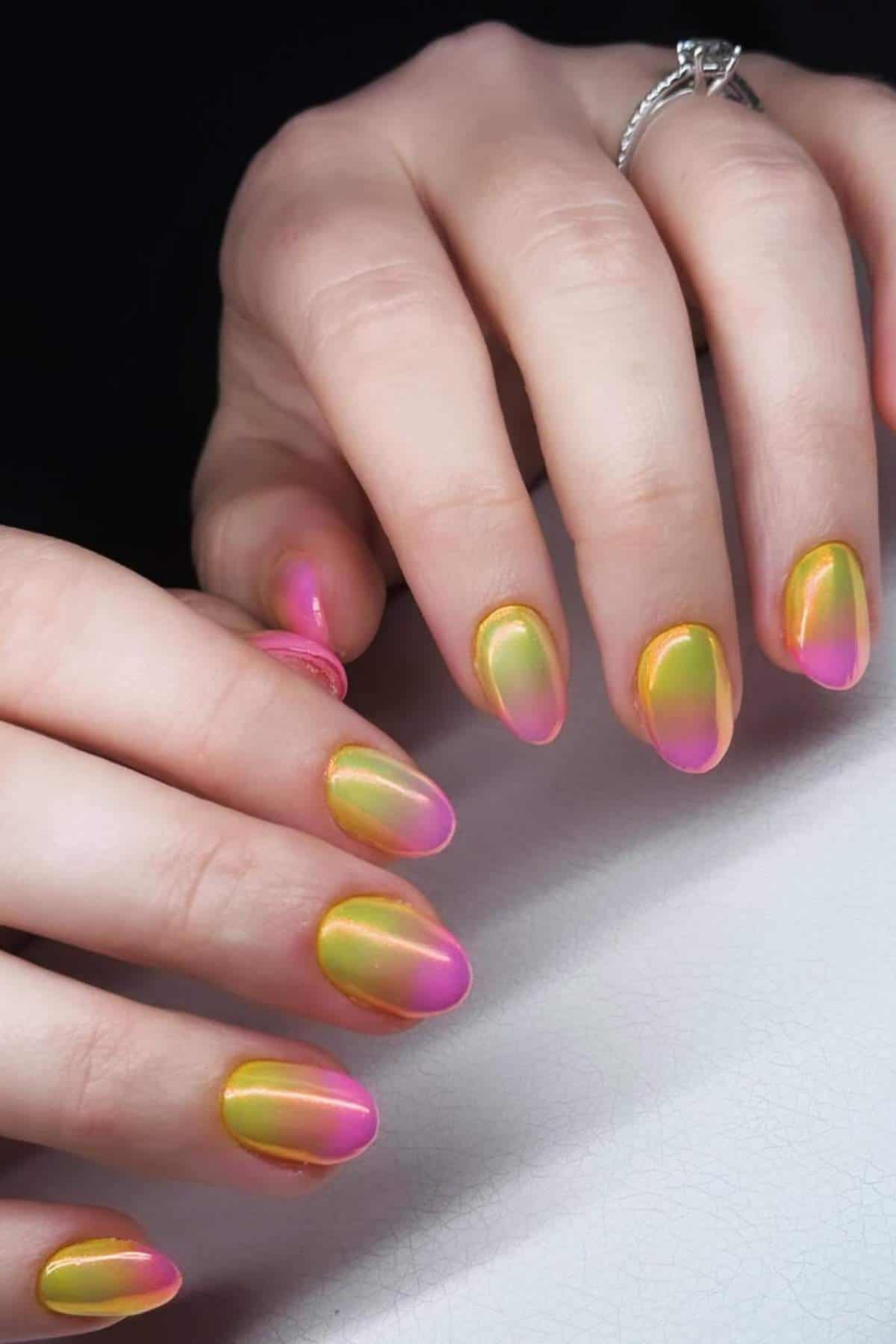 Close-up of hands with almond-shaped nails, featuring a gradient manicure in yellow, green, and pink shades with a glossy finish.