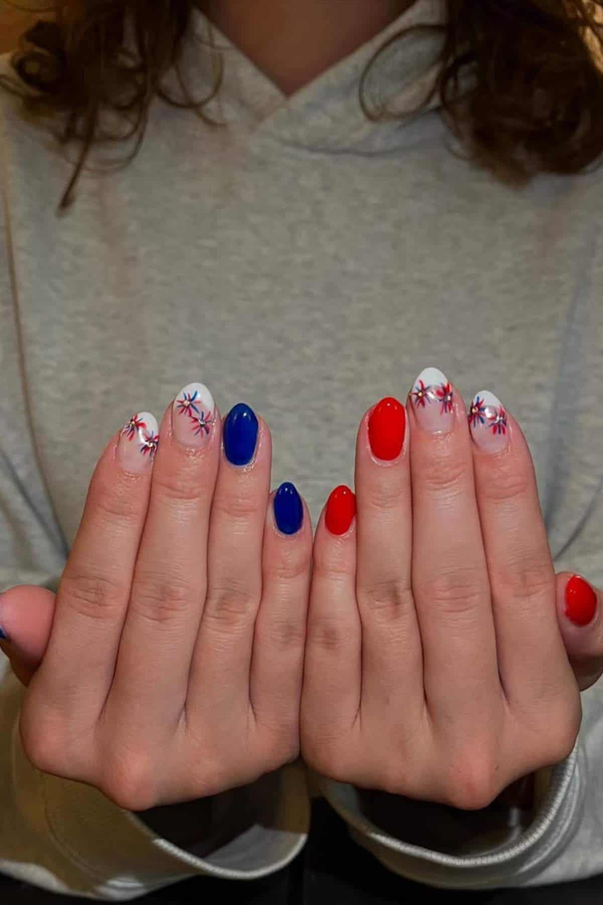 Hands with red, white, and blue nails featuring floral designs and solid colors.