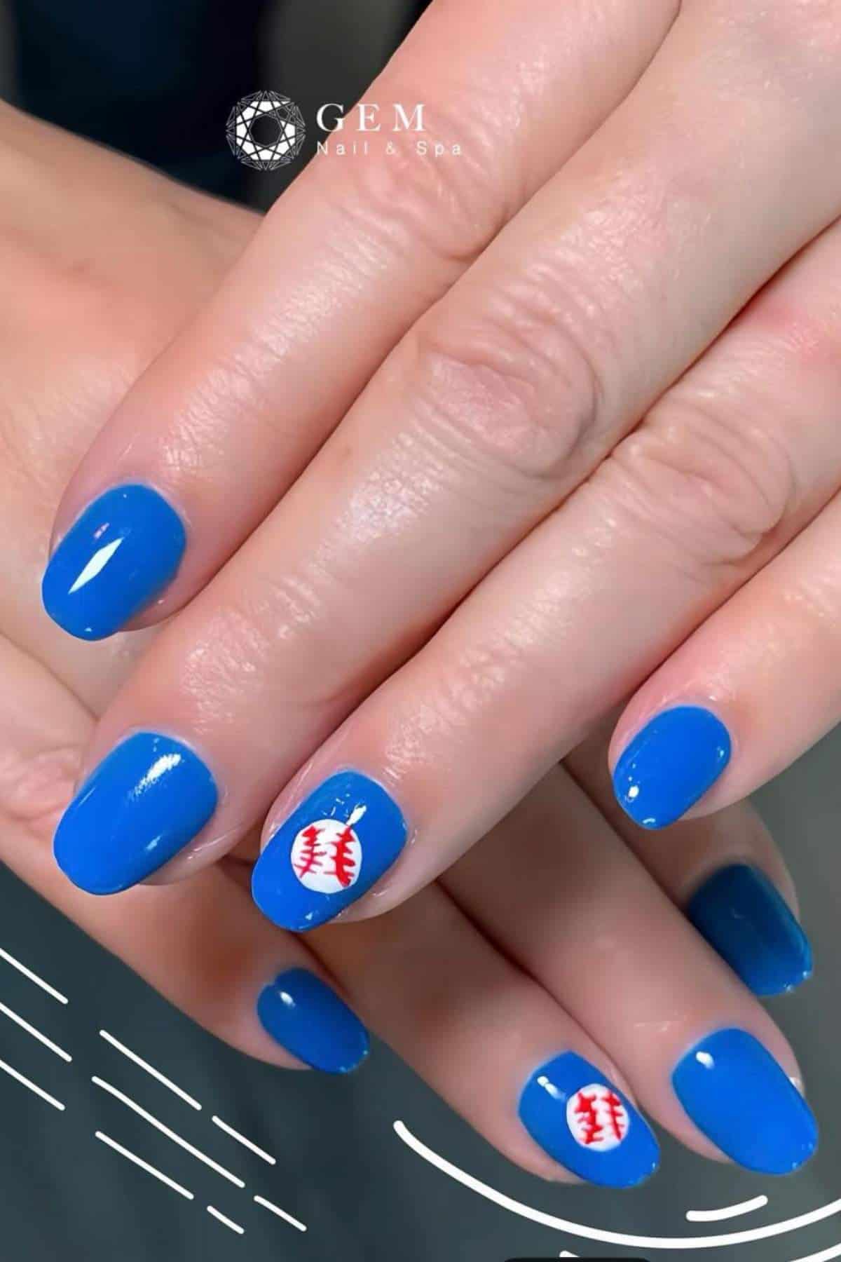 Hands with blue nail polish; ring fingernails feature a white round design with red stitching resembling a baseball.