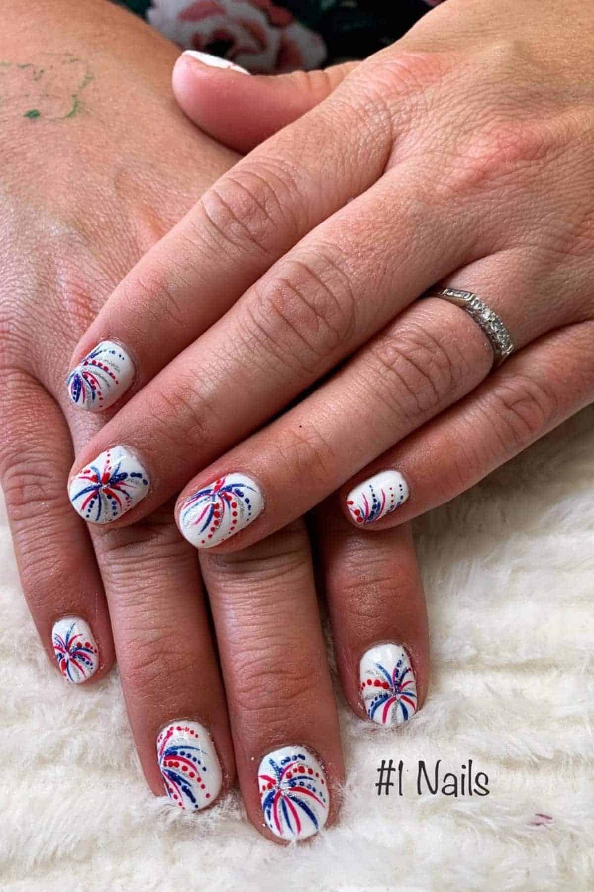 Close up of hands with white nails painted with red, white, and blue fireworks designs.