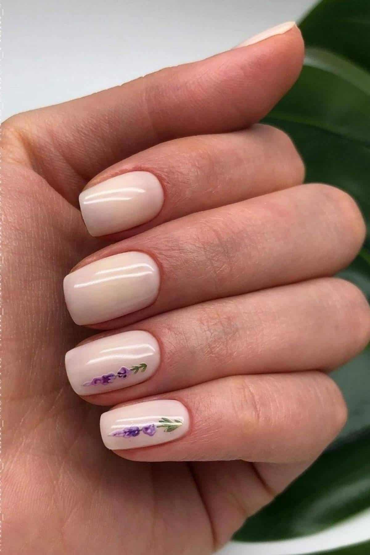 A hand with short, pale pink nails, two of which have small lavender sprigs painted on them.