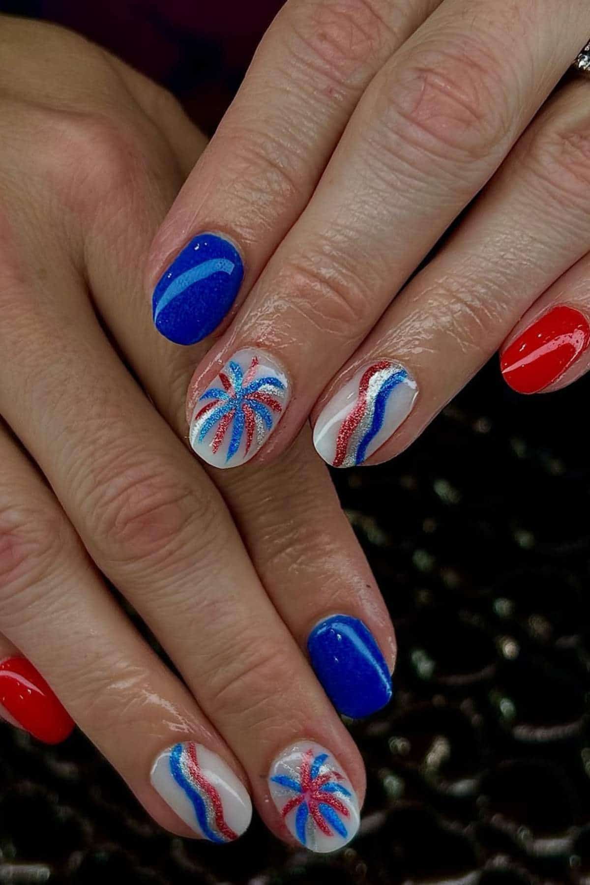 Hands with red, white, and blue patriotic-themed nails, featuring stripes and starburst designs.