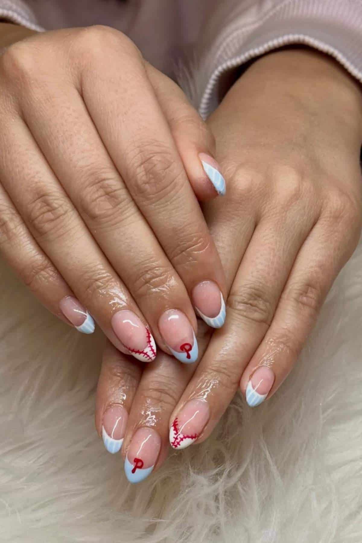 Hands with manicured nails featuring light blue French tips and two accent nails with red heart and squiggle designs, resting on a white textured surface.