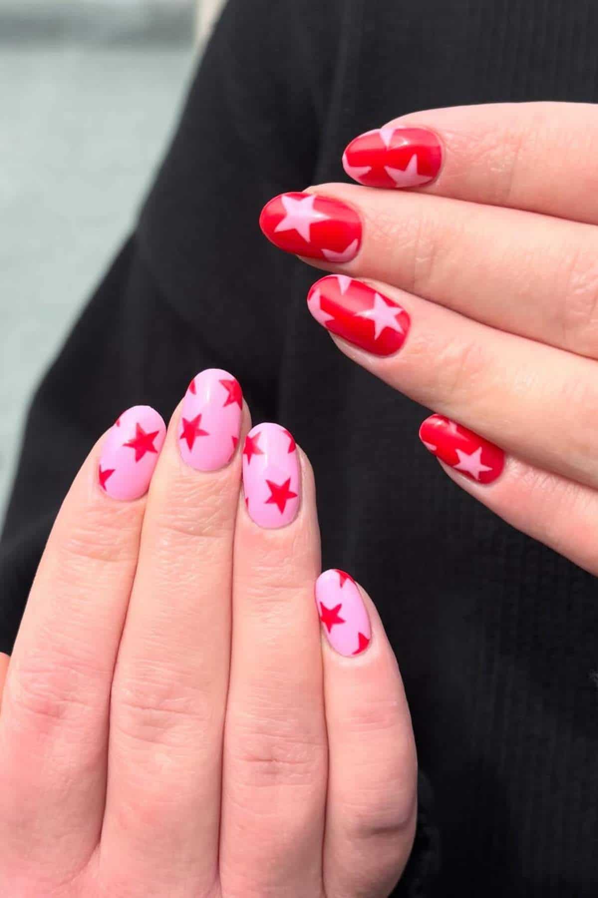Two hands with manicured nails; one hand has light pink nails with red stars, the other has red nails with pink stars.