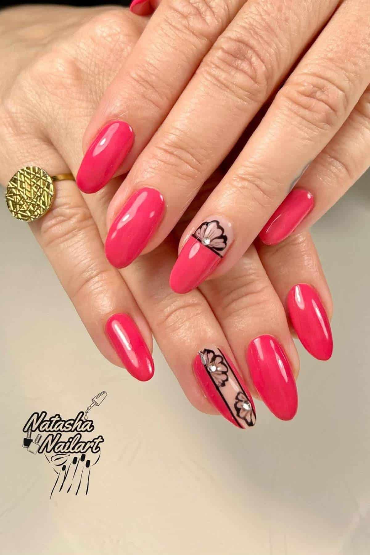 Hands with oval-shaped, bright pink manicured nails; one nail on each hand features a black and white floral design. A gold patterned ring is worn on one finger.