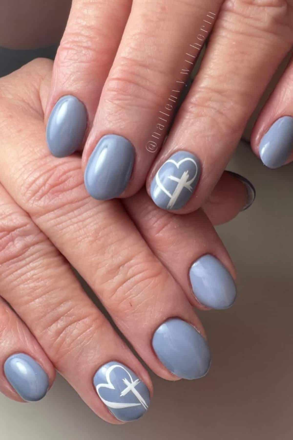 Hands with short, oval-shaped nails painted in glossy lavender polish; two accent nails feature a white outlined heart and line design.