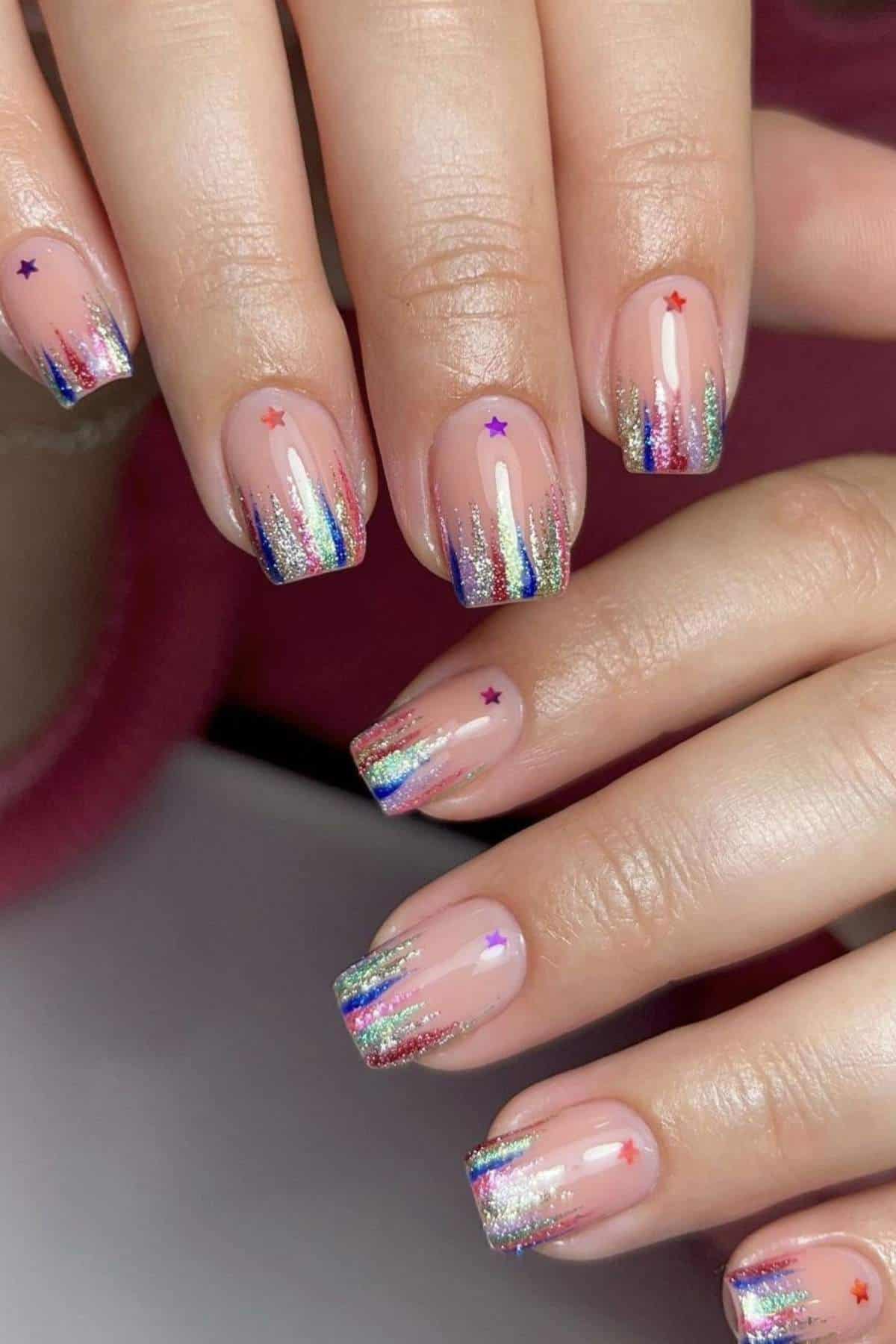Close-up of hands with nails painted in a rainbow glitter gradient at the tips and small colorful star stickers on each nail.