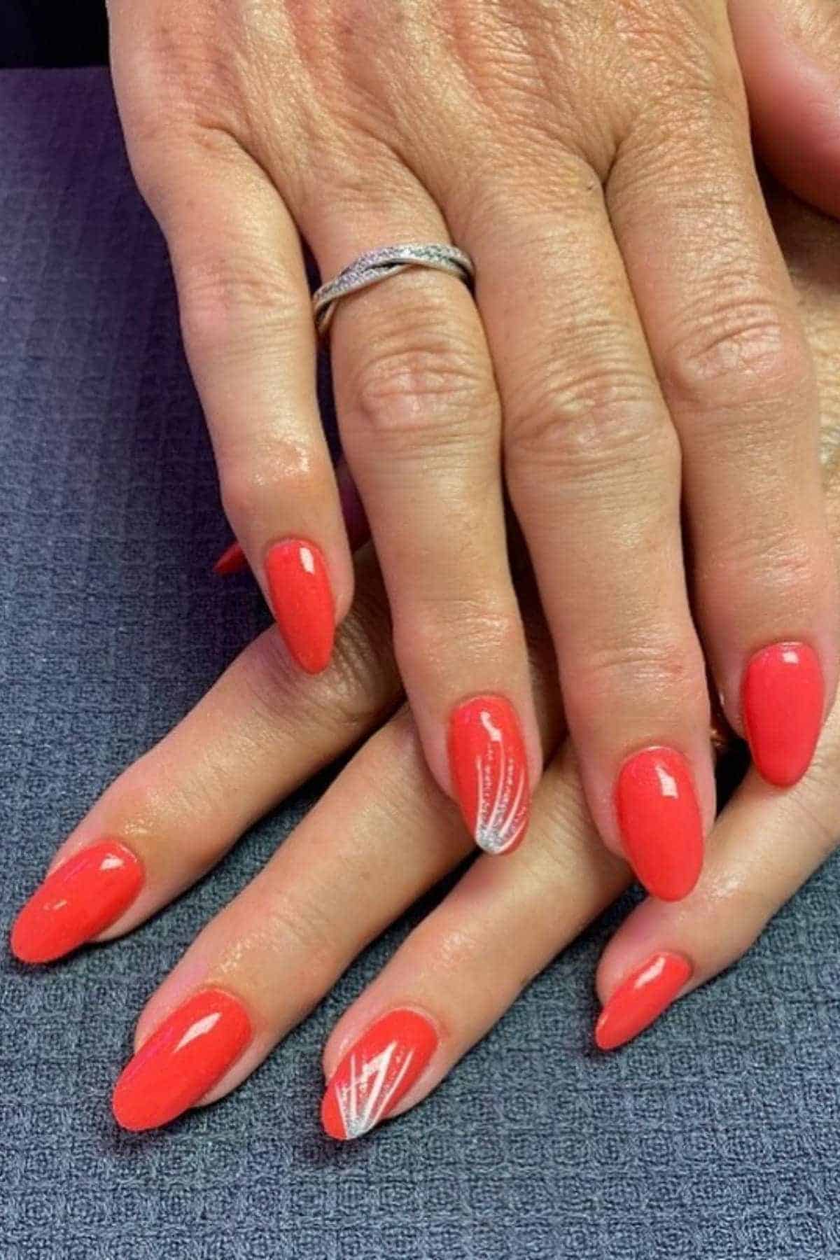 Hands with short, almond-shaped nails painted bright red; one nail on each hand has a white abstract line design.