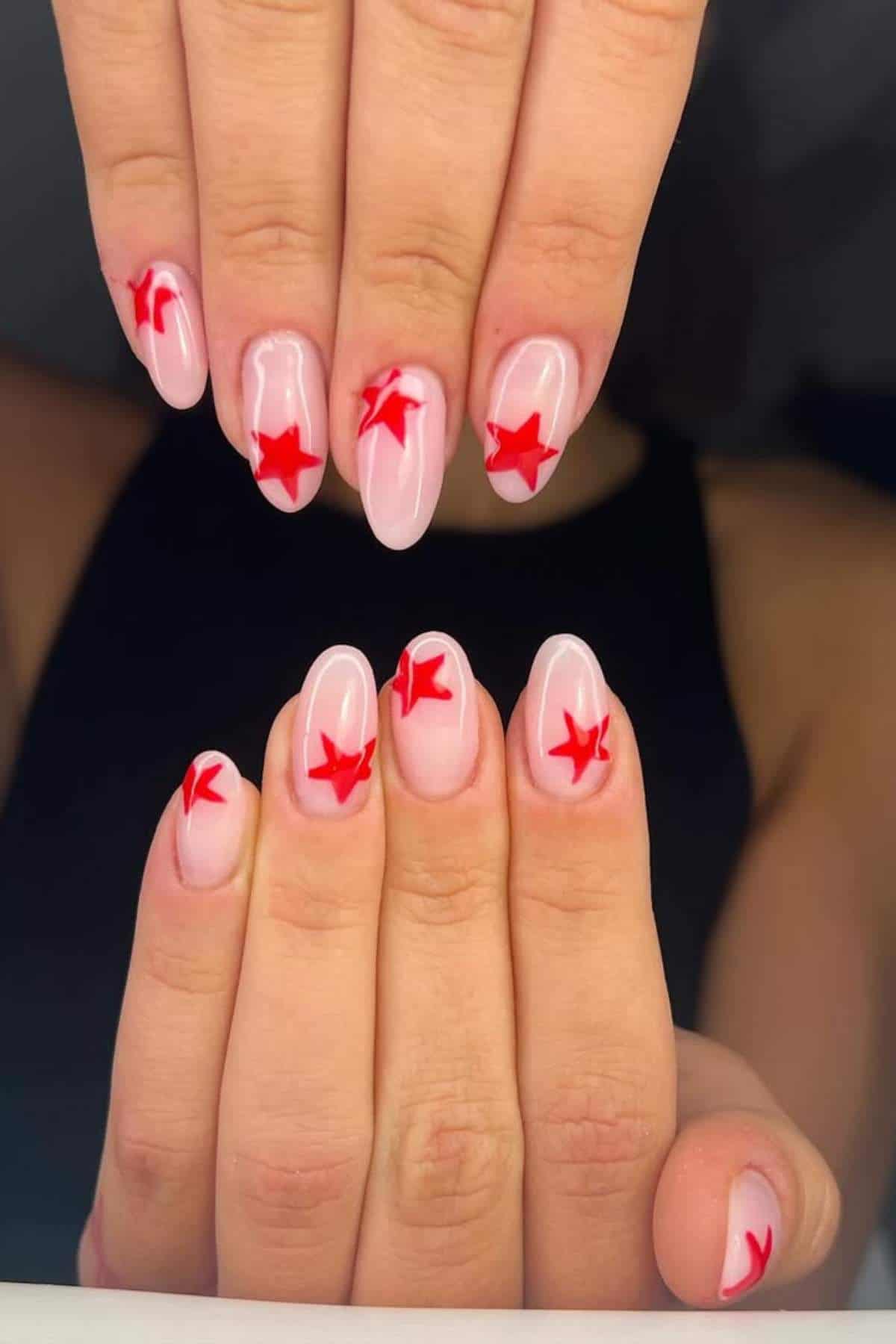 Hands with almond-shaped nails painted light pink, each featuring a red star design on the tips and centers.