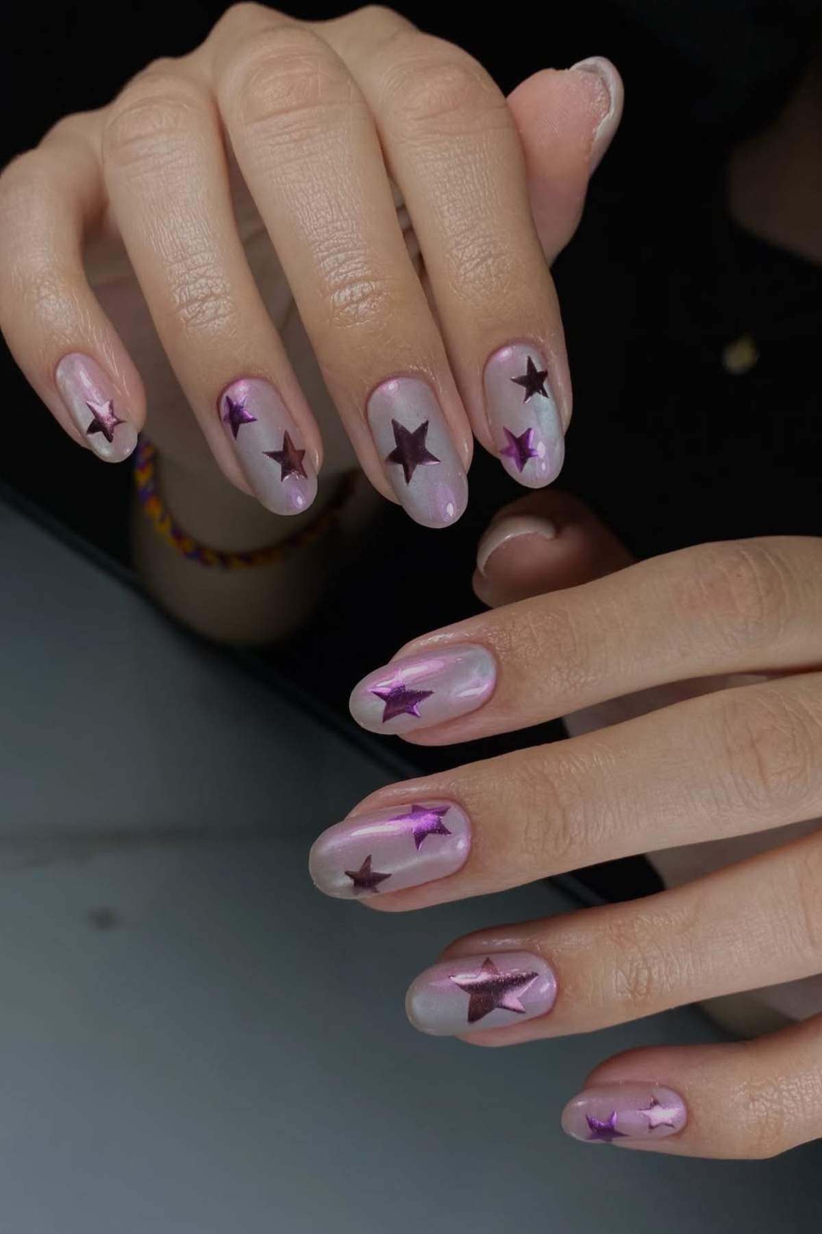 Two hands with manicured nails featuring a pinkish base and purple star-shaped decorations on each nail.