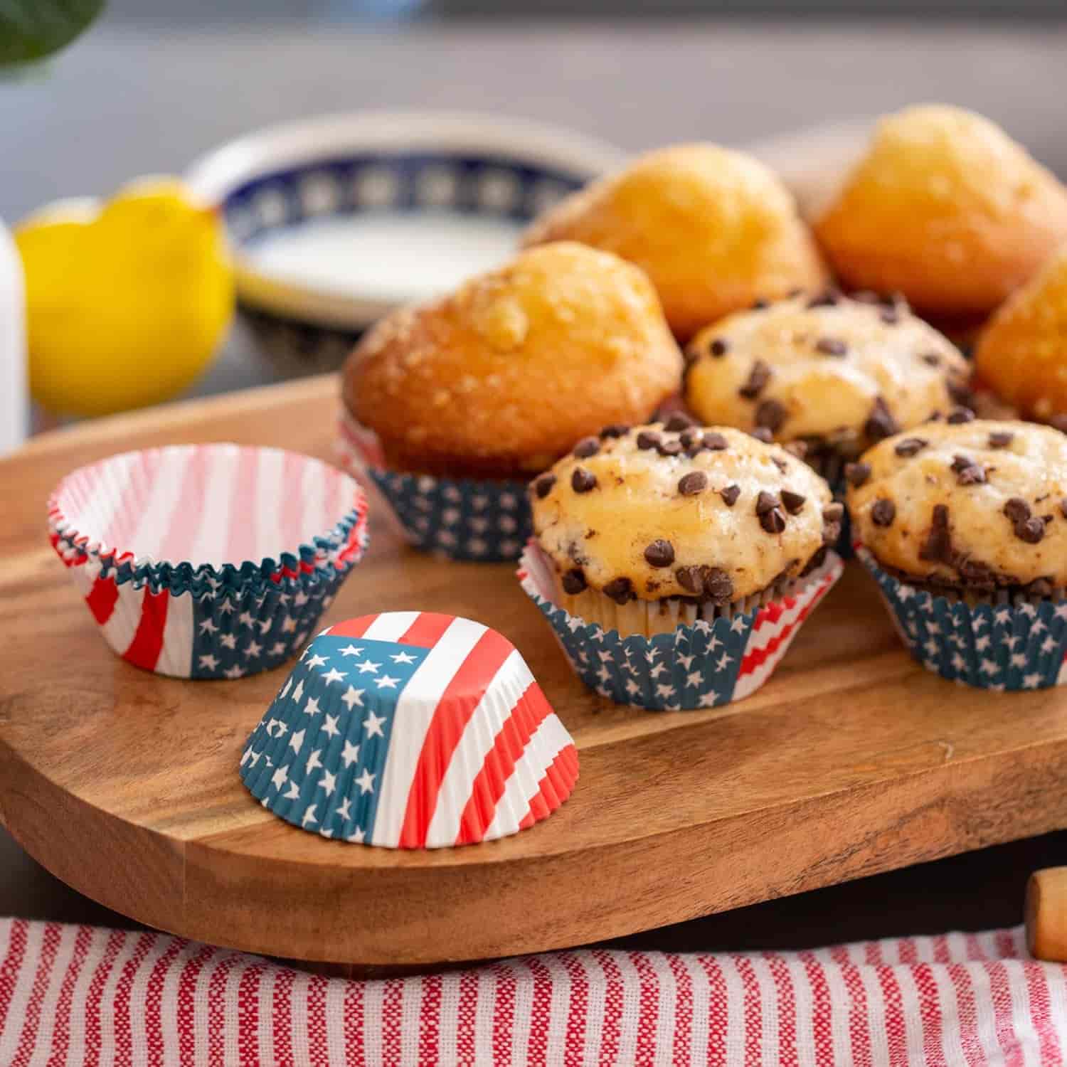 Assorted muffins, some with chocolate chips, on a wooden board with red, white, and blue American flag-themed cupcake liners.