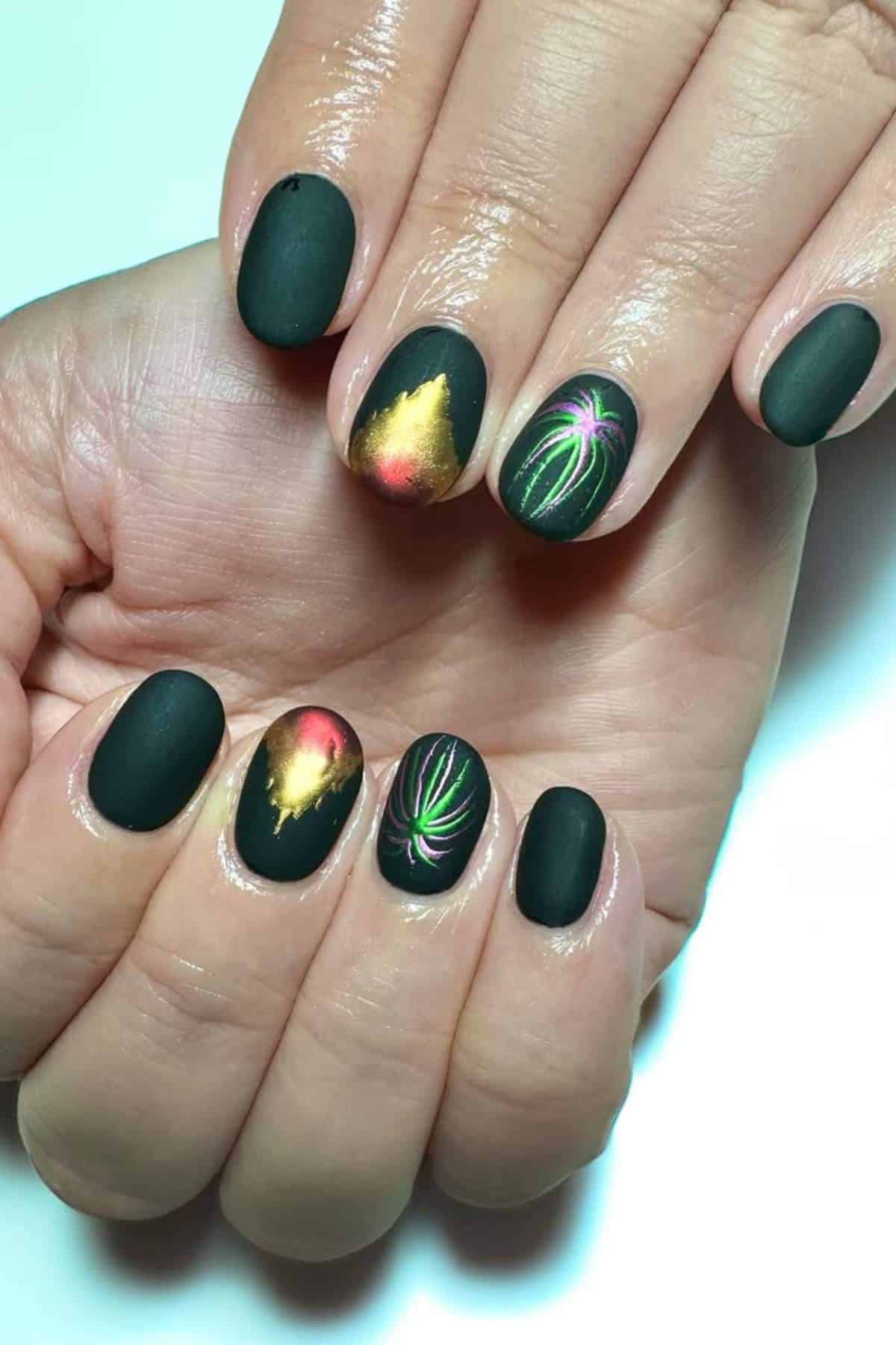 Hands with black matte nail polish, some nails featuring colorful designs resembling fireworks and gold foil accents.