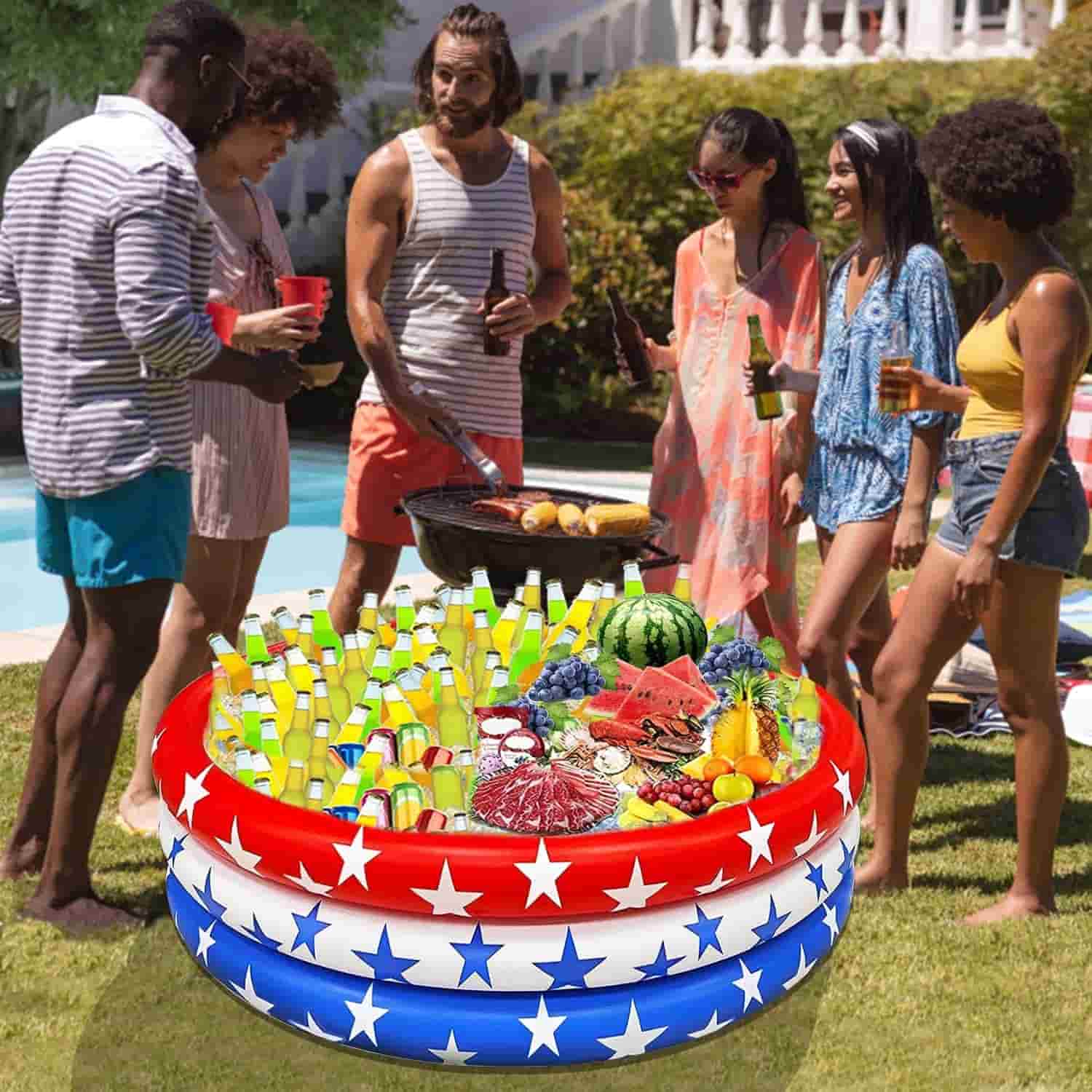 Six people stand near a pool, socializing and grilling food. In the foreground, a red, white, and blue inflatable pool is filled with drinks, fruit, and snacks.