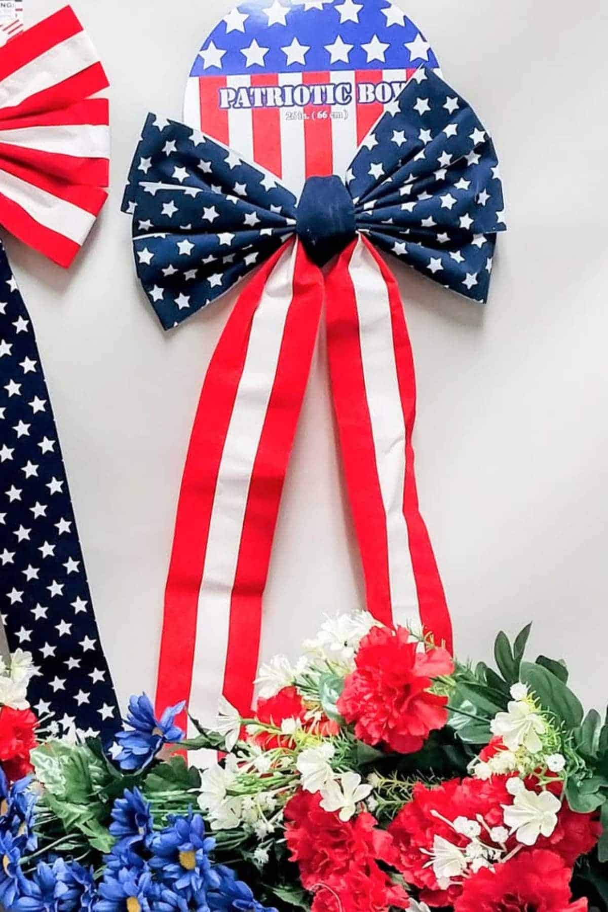 Red, white, and blue bow with stars and stripes pattern displayed above a bouquet of red, white, and blue artificial flowers.