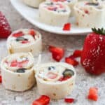 Strawberry and blueberry tortilla roll-ups on a speckled countertop, with sliced strawberries and powdered sugar sprinkled on top.