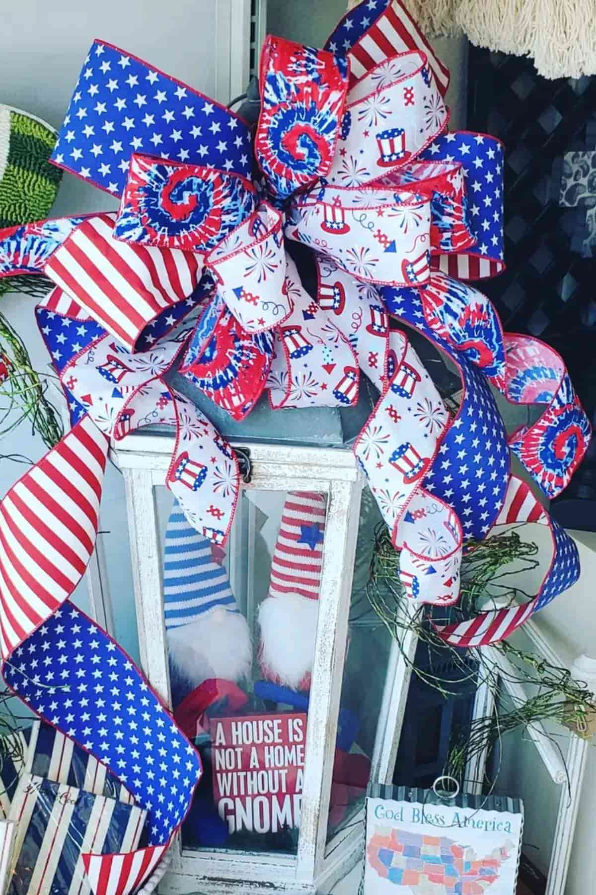A decorative lantern adorned with patriotic ribbons and two gnomes sits on display.