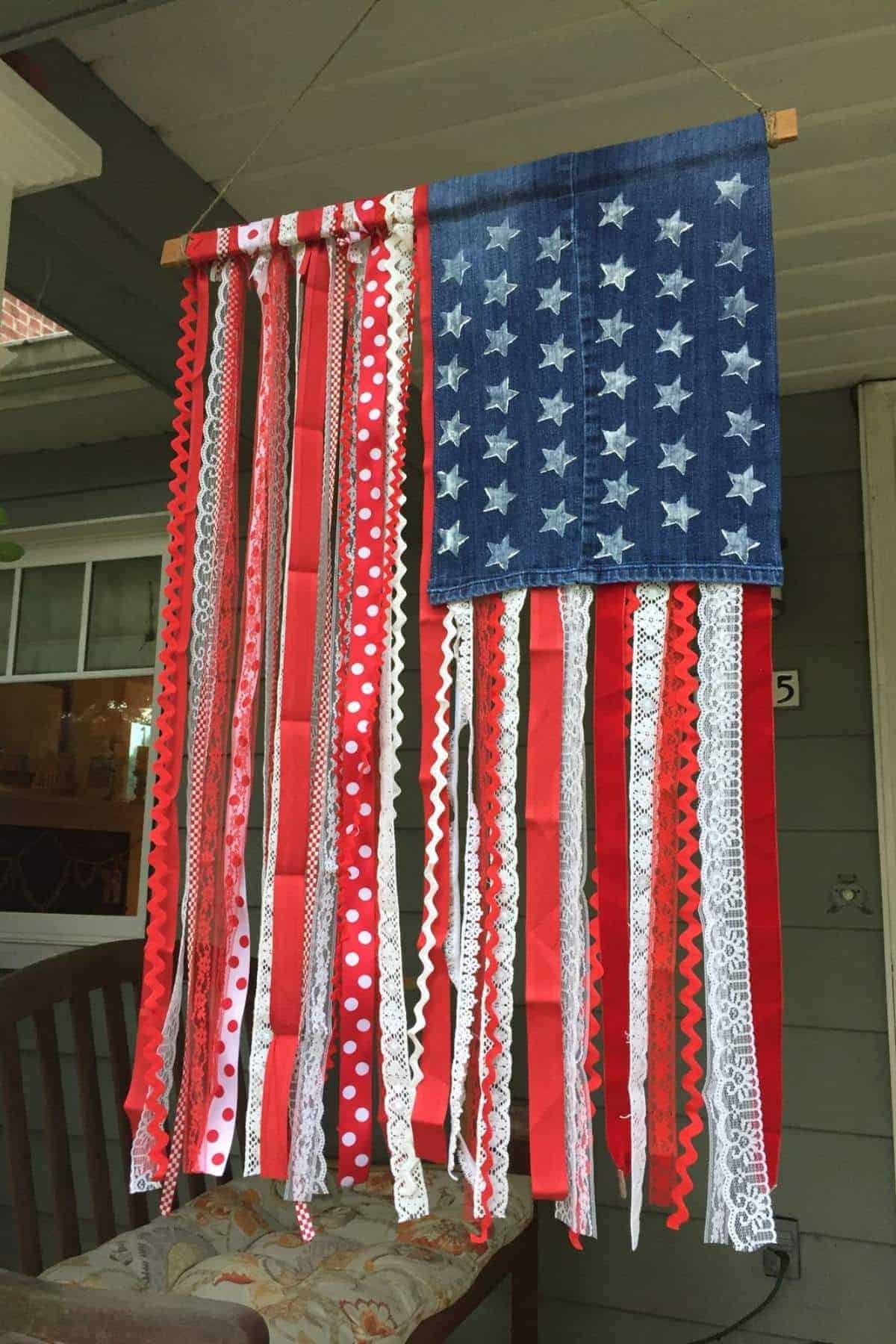 A homemade American flag decoration with a blue denim square and white stars, and red, white, and lace ribbons hanging as stripes.