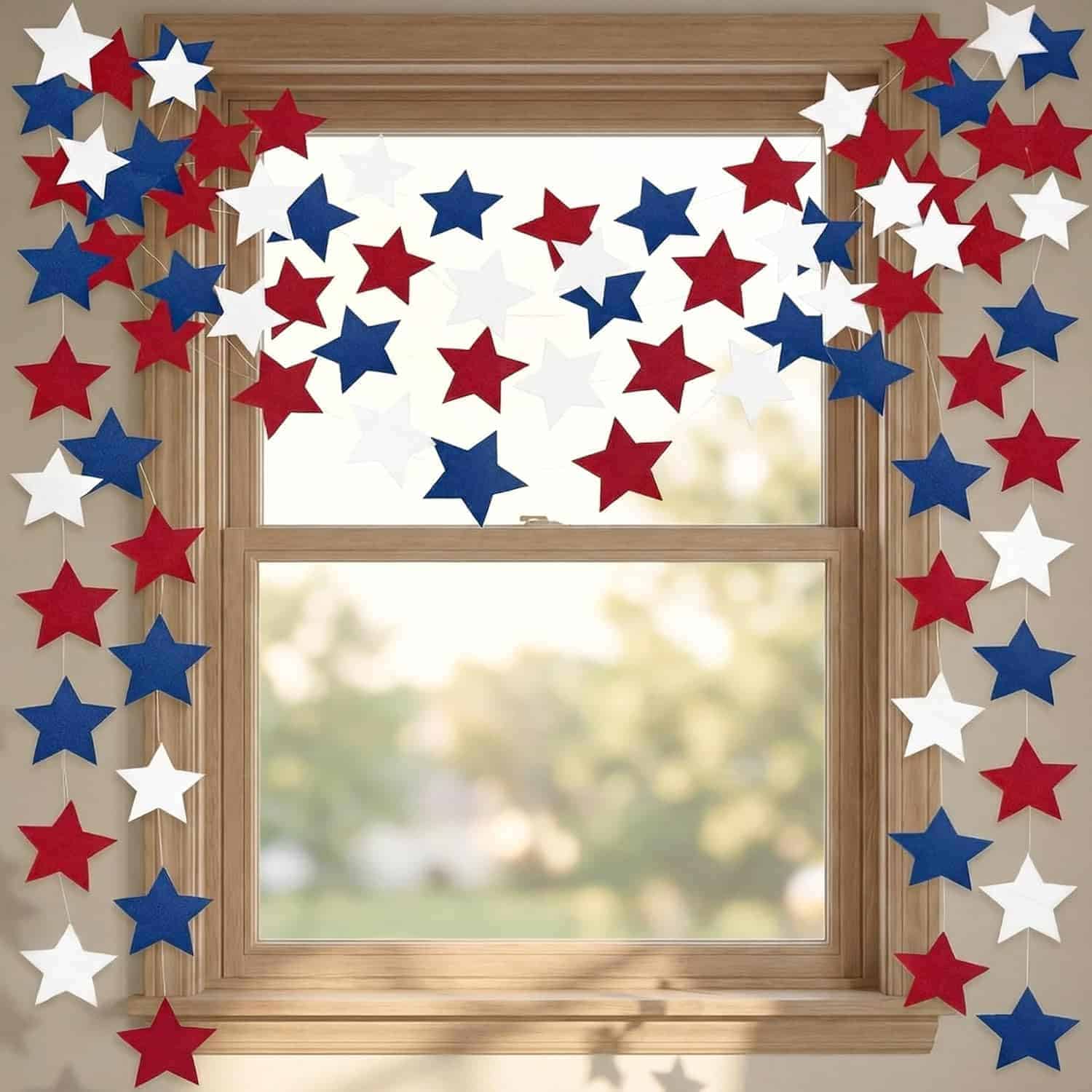 Red, white, and blue star-shaped decorations hang around a wooden-framed window with sunlight coming through.
