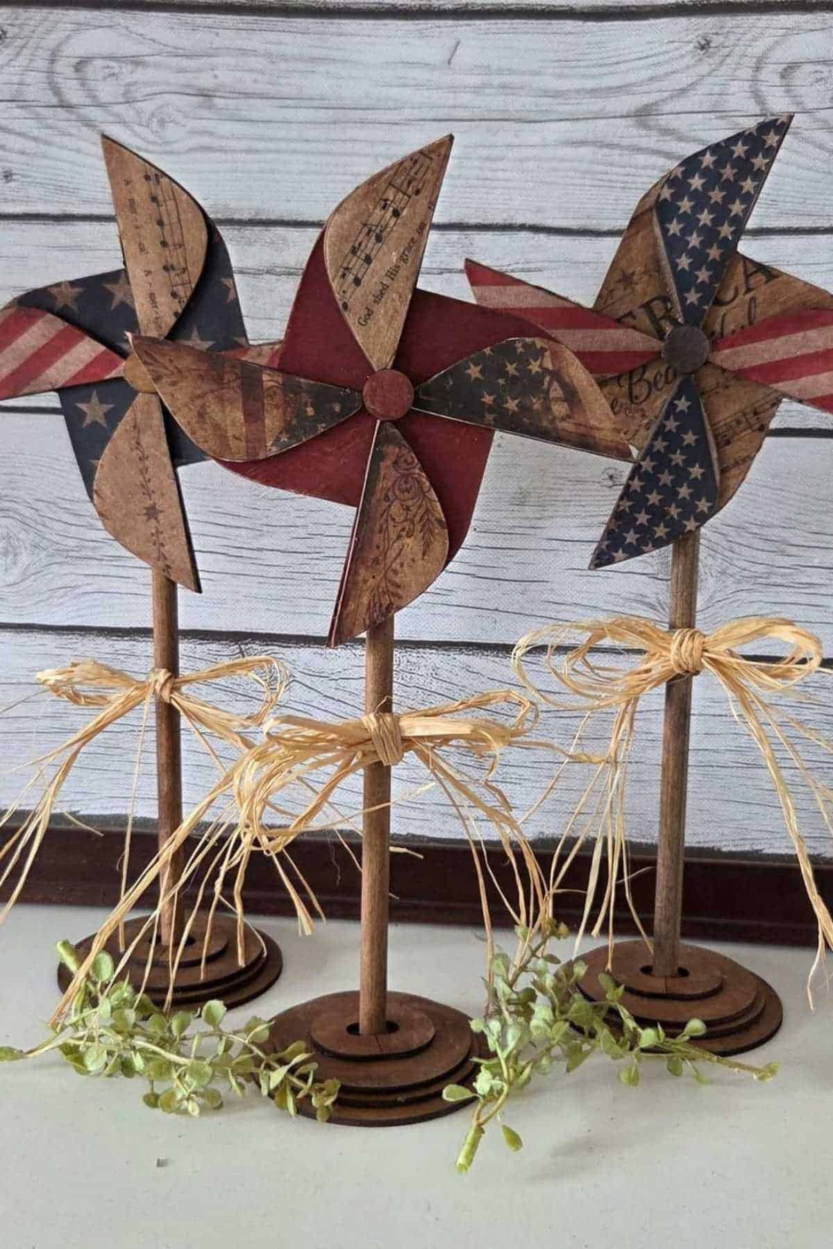 Three decorative pinwheels with patriotic designs, stands, and raffia bows.
