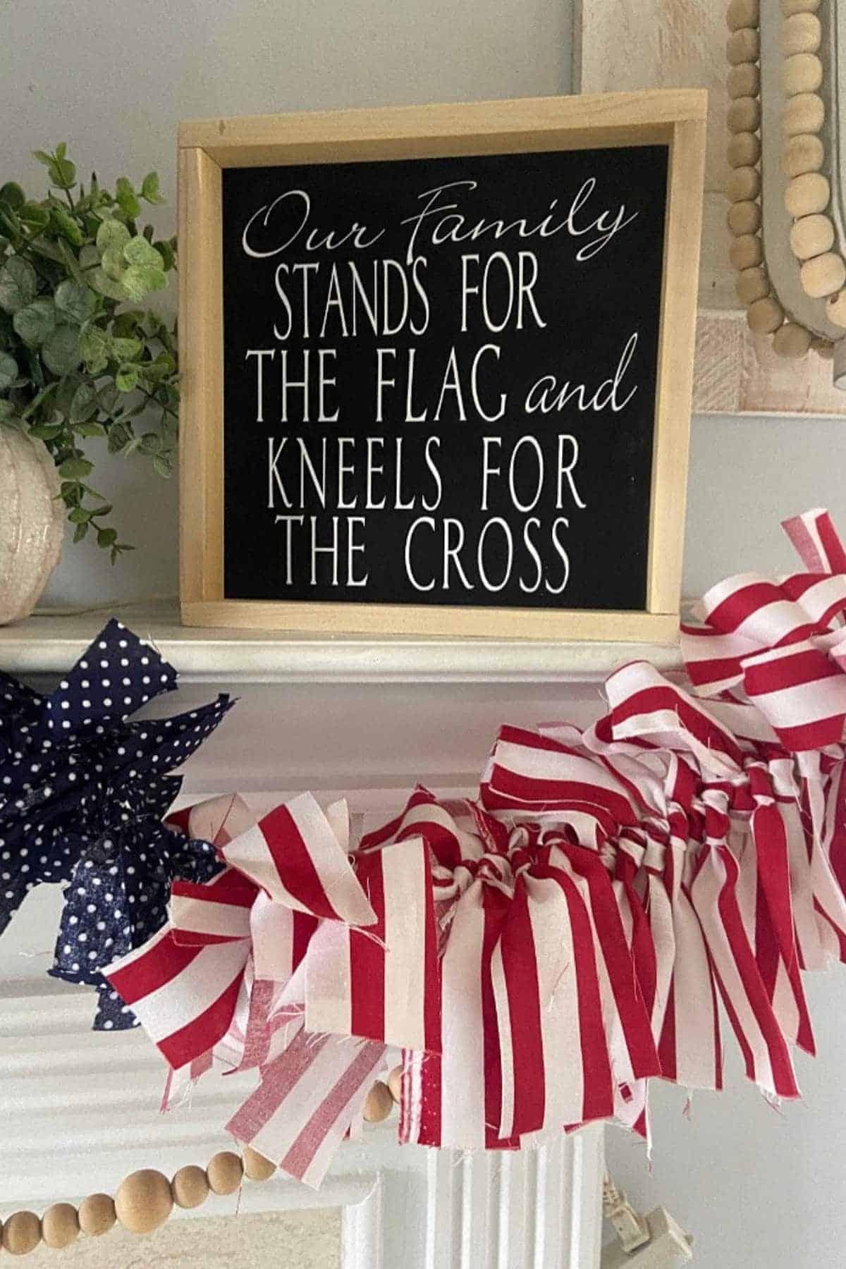 A sign reading "Our family stands for the flag and kneels for the cross" is displayed above a mantel decorated with red, white, and blue fabric garland.