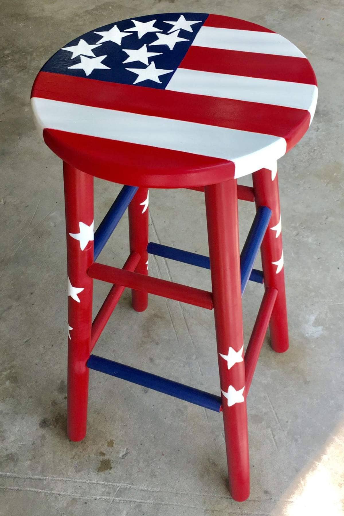 A wooden bar stool painted with the American flag design, featuring red, white, and blue stripes and white stars.