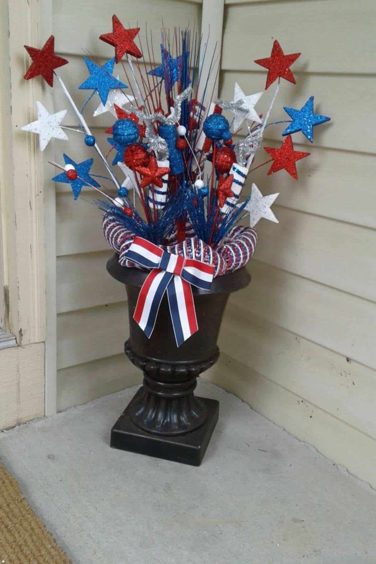 A patriotic floral arrangement with glitter stars in red, white, and blue, adorned with a large ribbon bow.